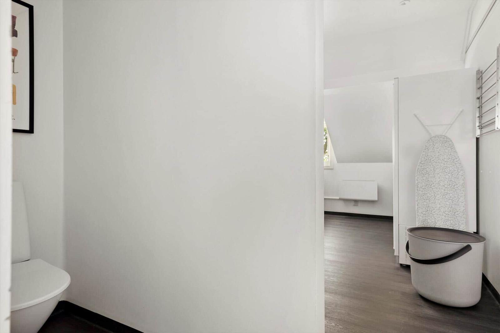 Badezimmer mit Toilette und Blick in Wohnbereich mit Heizung und Bügeltisch.