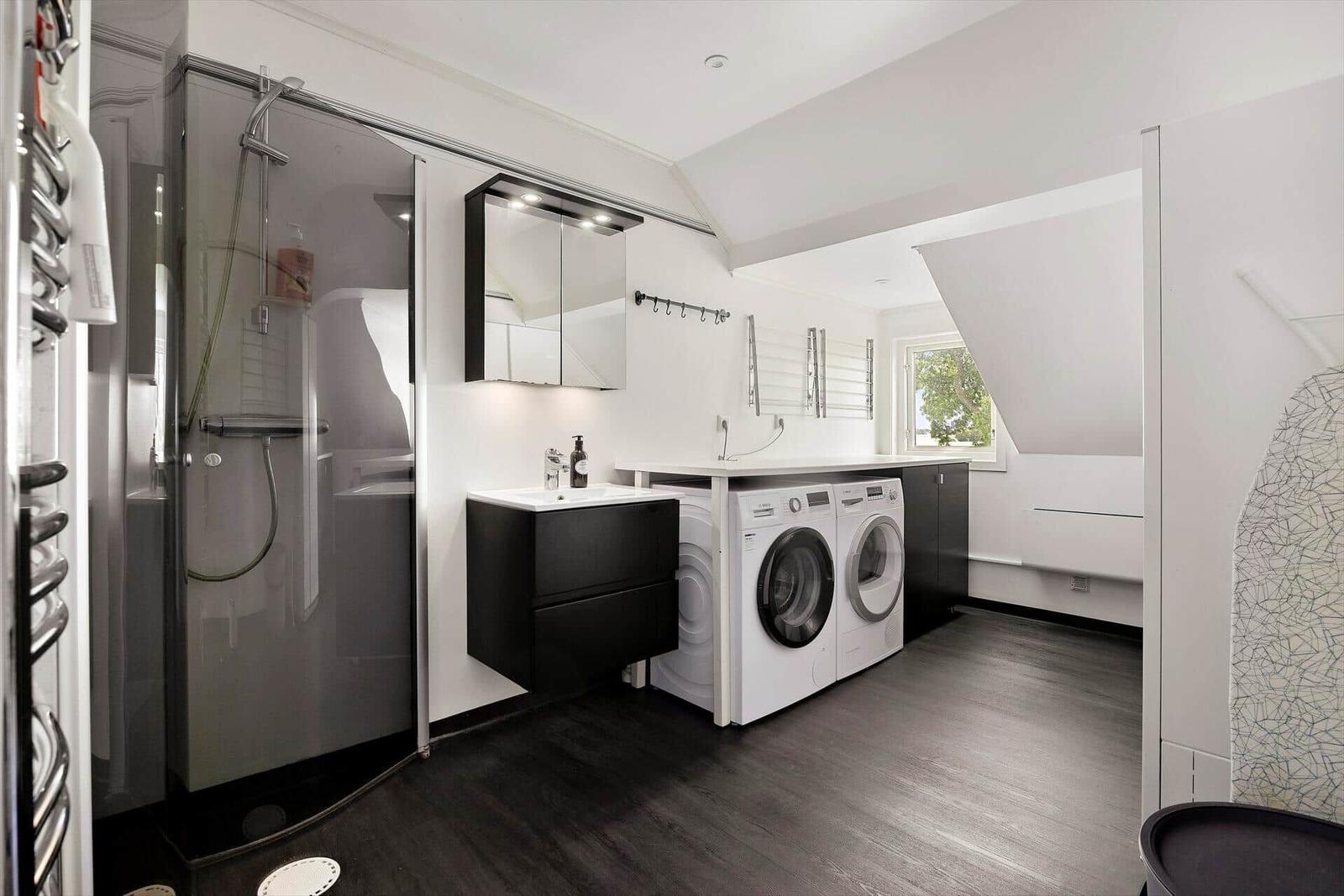 Dusche, Waschbecken und Waschmaschine in einem Raum mit dunklem Boden und weißer Wand.