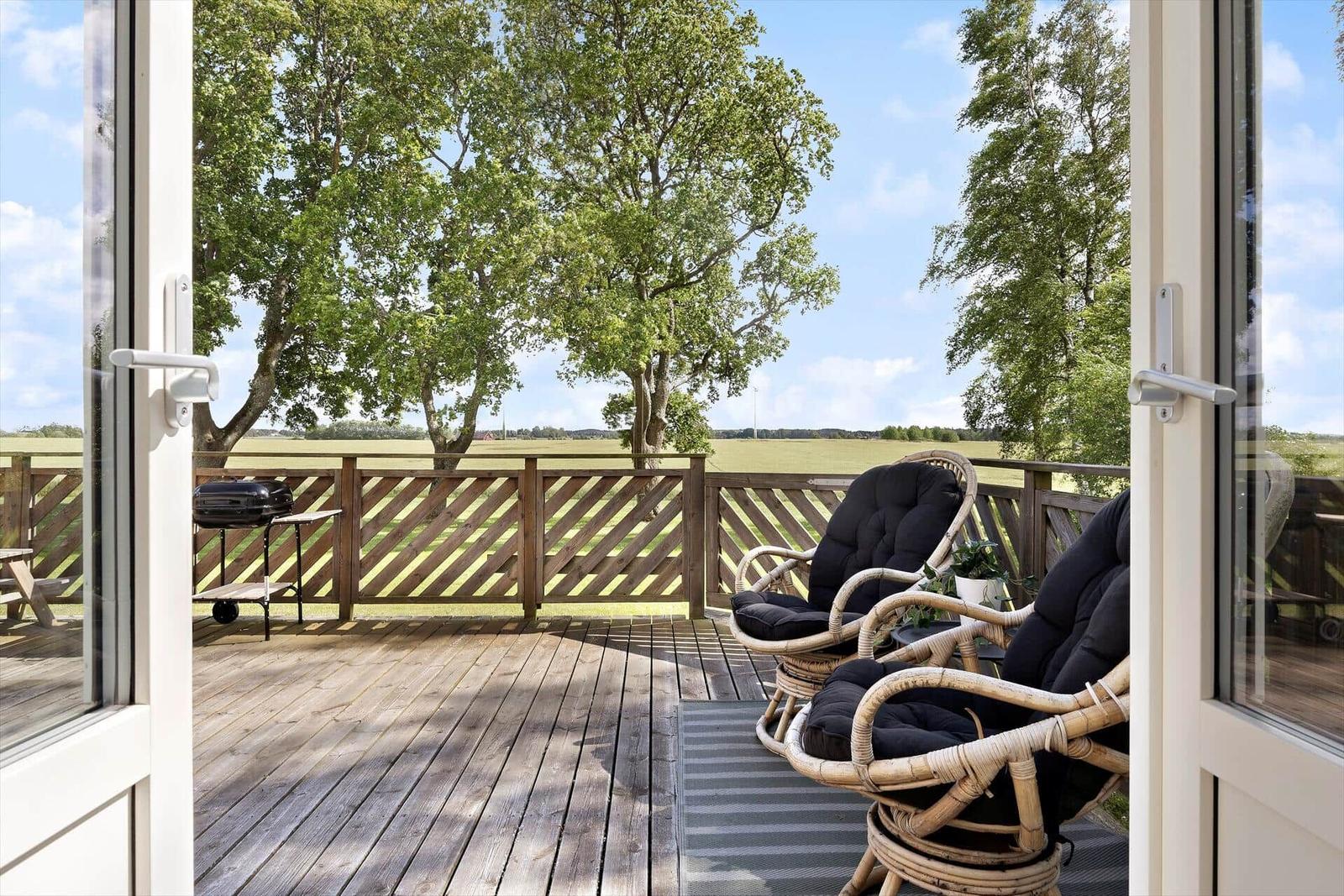 Terrasse mit Rattanstühlen, Grill und Blick auf Felder und Bäume.