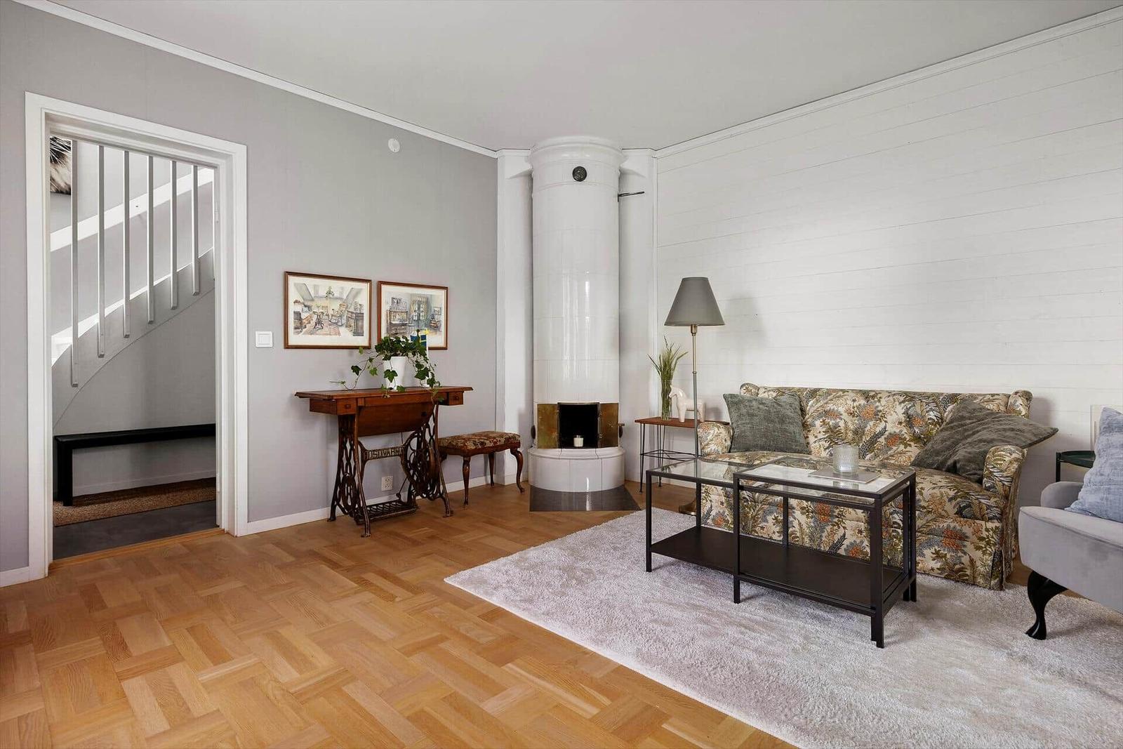 Wohnzimmer mit Sofa, Kamin und Holzboden. Tür führt zur Treppe.