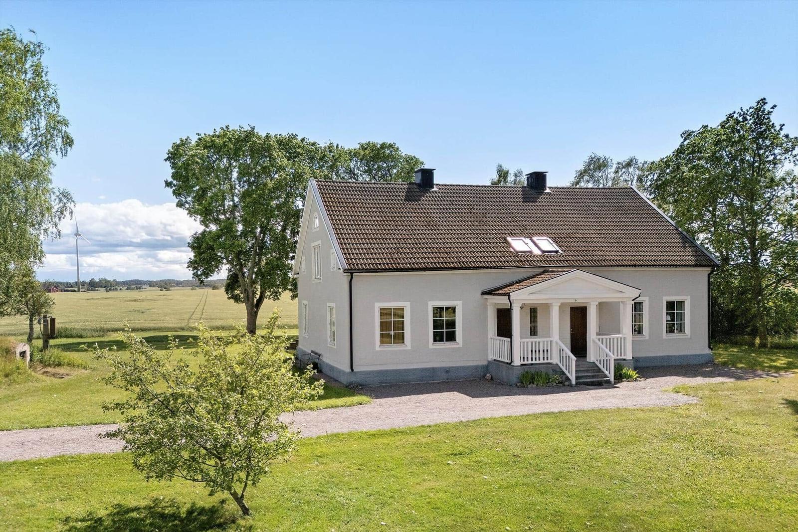 Ein weißes Haus mit braunem Dach steht in einer grünen Landschaft.