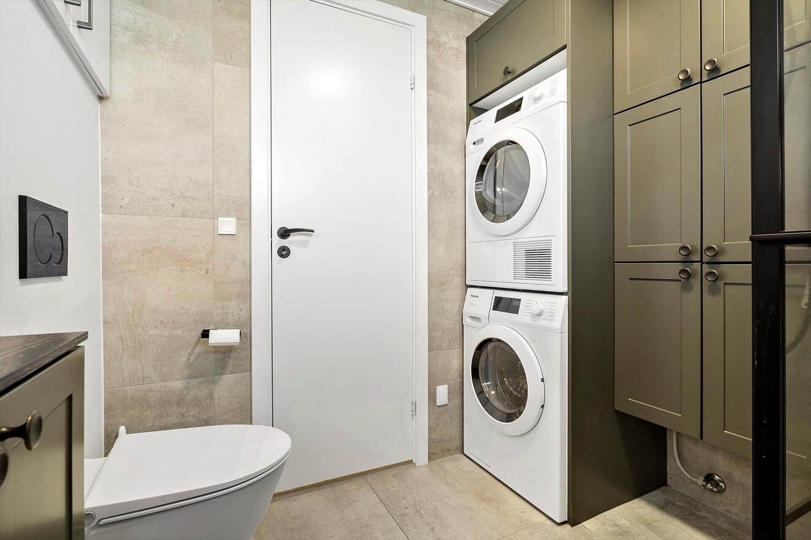 Washing and drying machine in a room with toilet and cabinets.