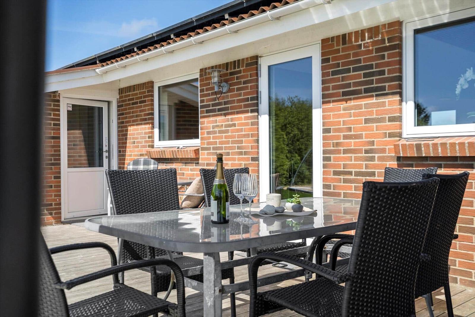Terrace with table, chairs, and bottle of champagne in front of brick house.