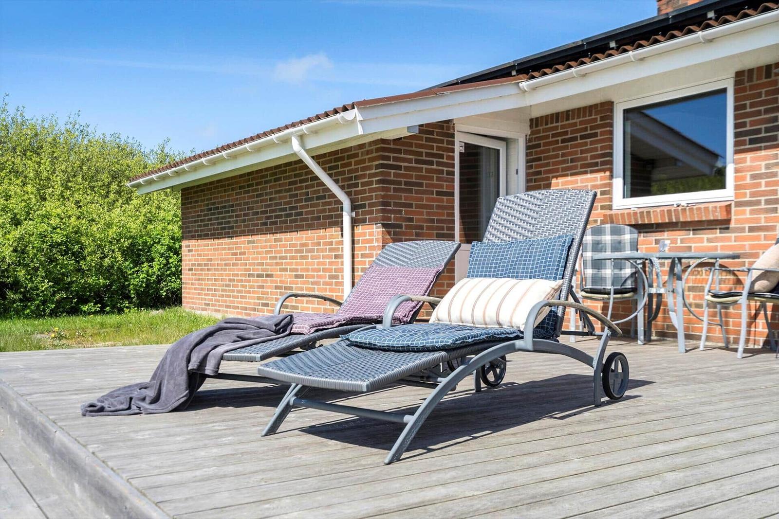Deck with lounge chairs and table in front of a brick house.