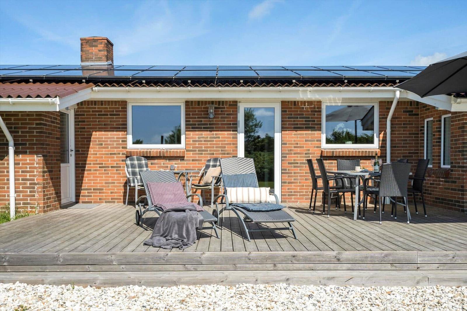 Deck with loungers and table, house with solar panels and brick facade.
