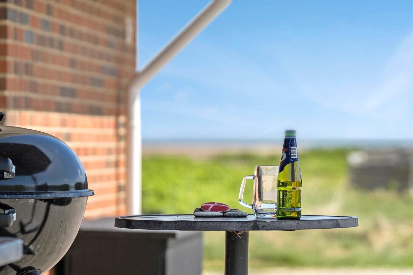 On the terrace, a table holds a bottle, a glass, and a grill.