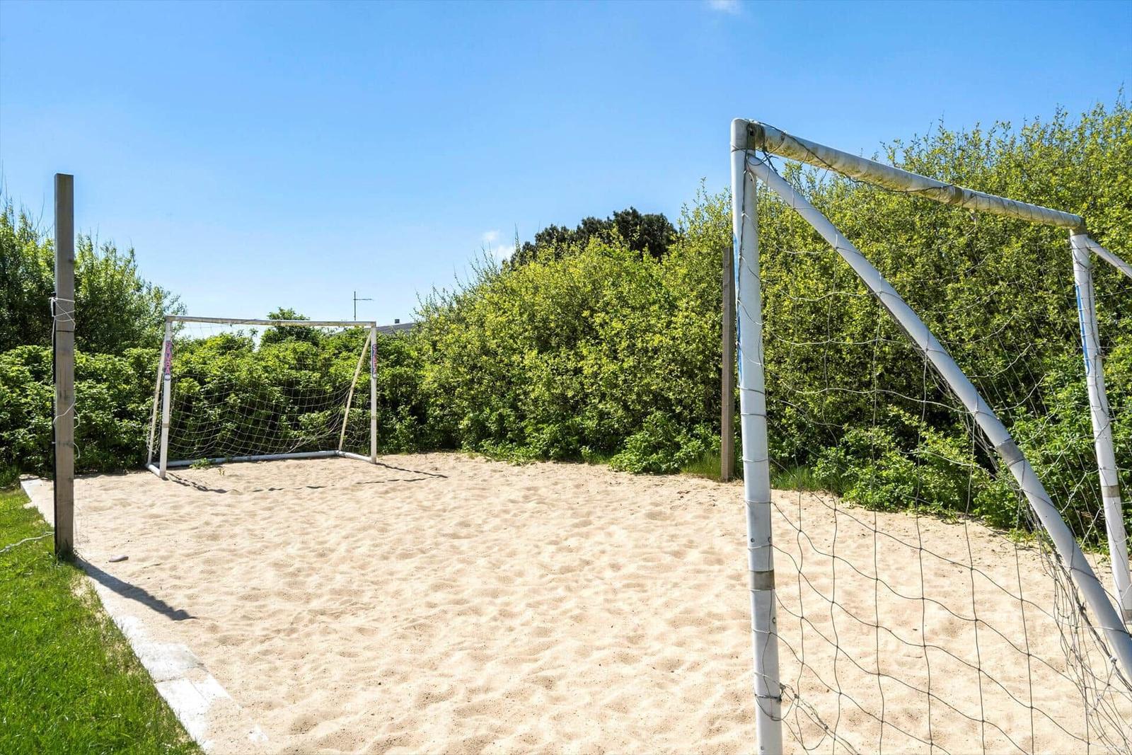 Playground with sandy area and two goals surrounded by greenery.