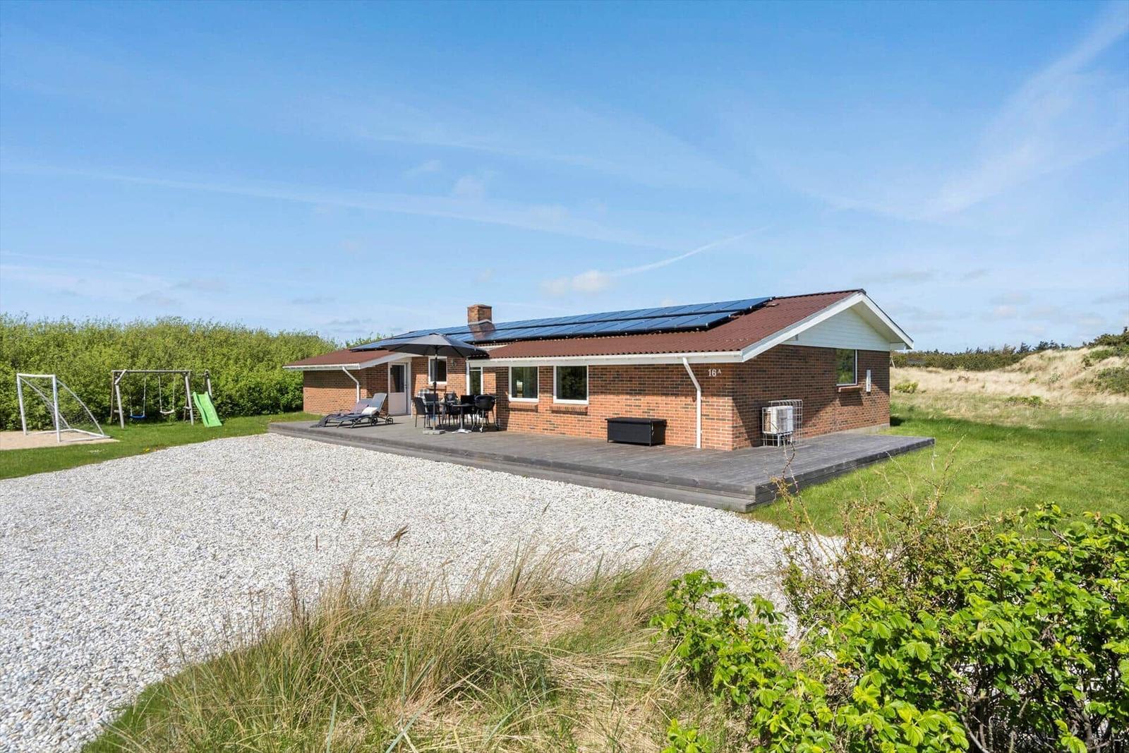 Single-story house with terrace, grill, and playground in grassland.