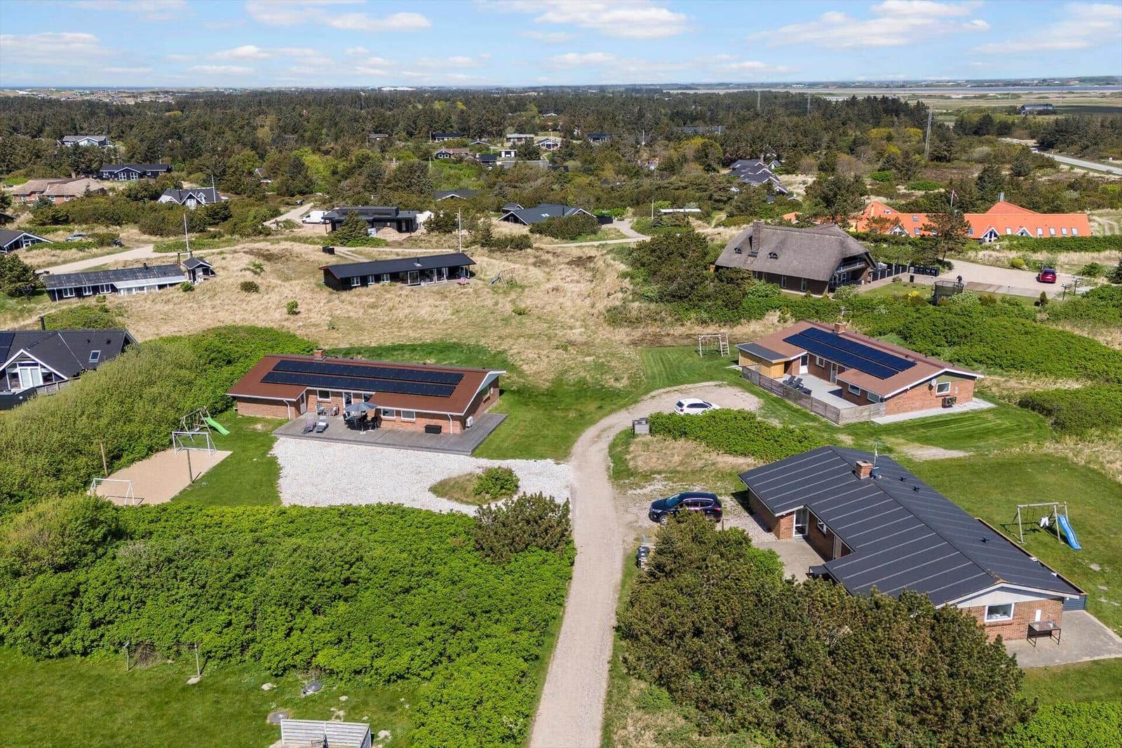 Aerial view of holiday homes with solar panels and playgrounds in green surroundings.