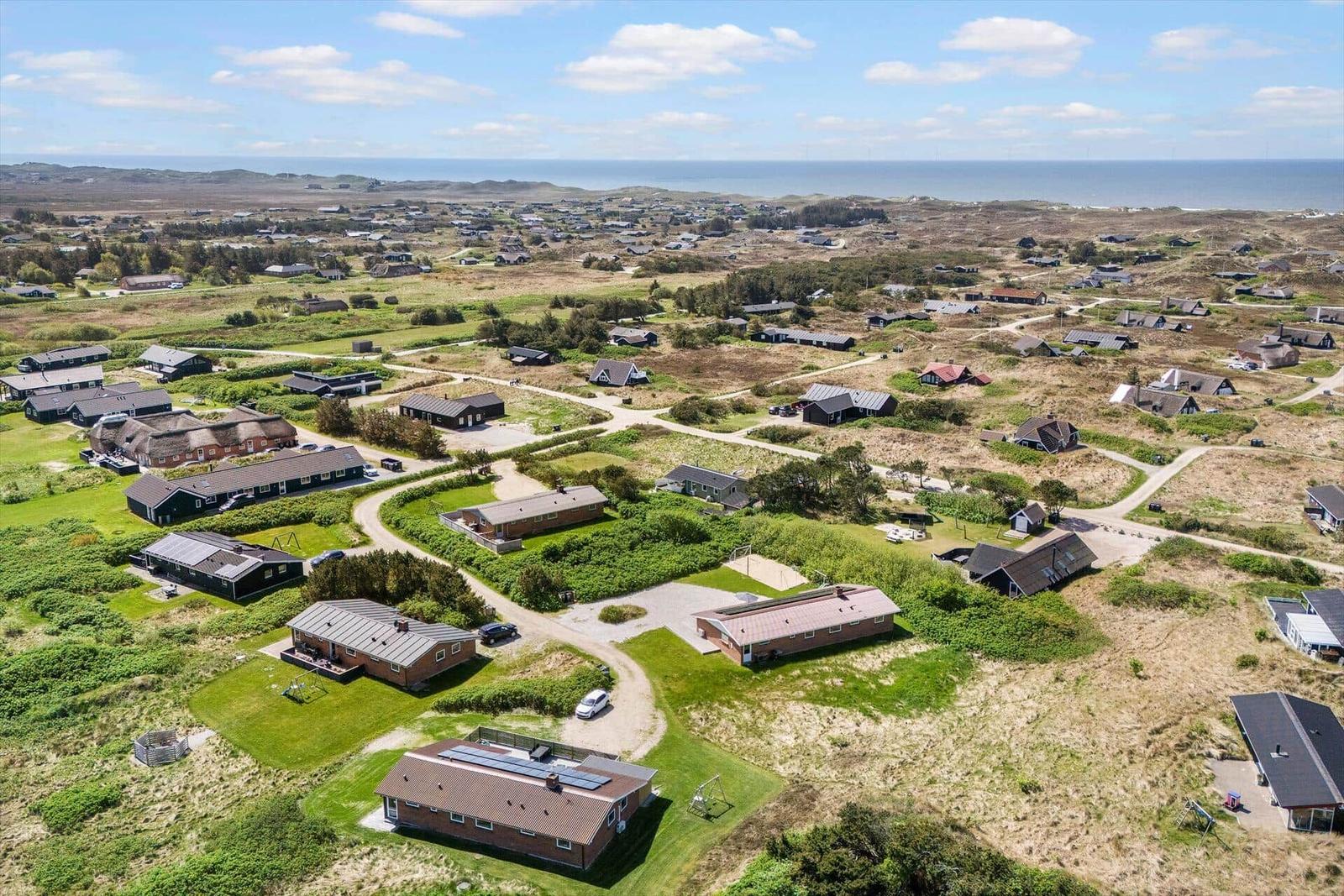 Aerial view of holiday homes near the sea with green lawns and winding paths.