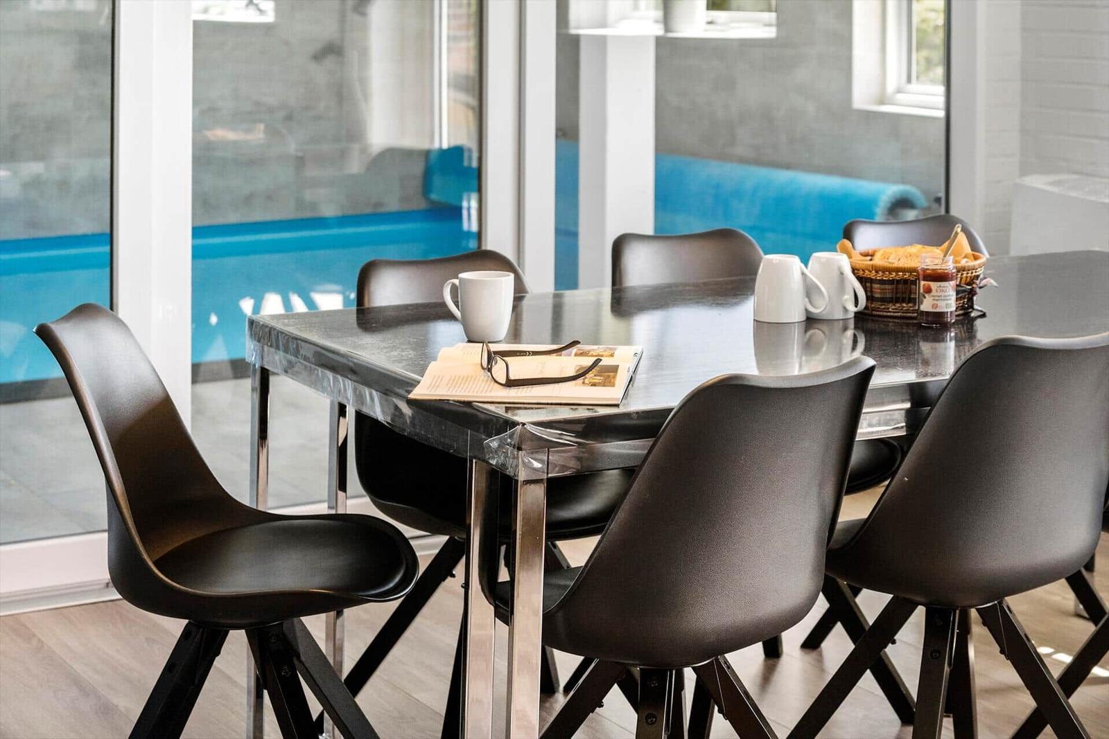 Dining table with six chairs, mugs, and bread basket. Access to pool area.