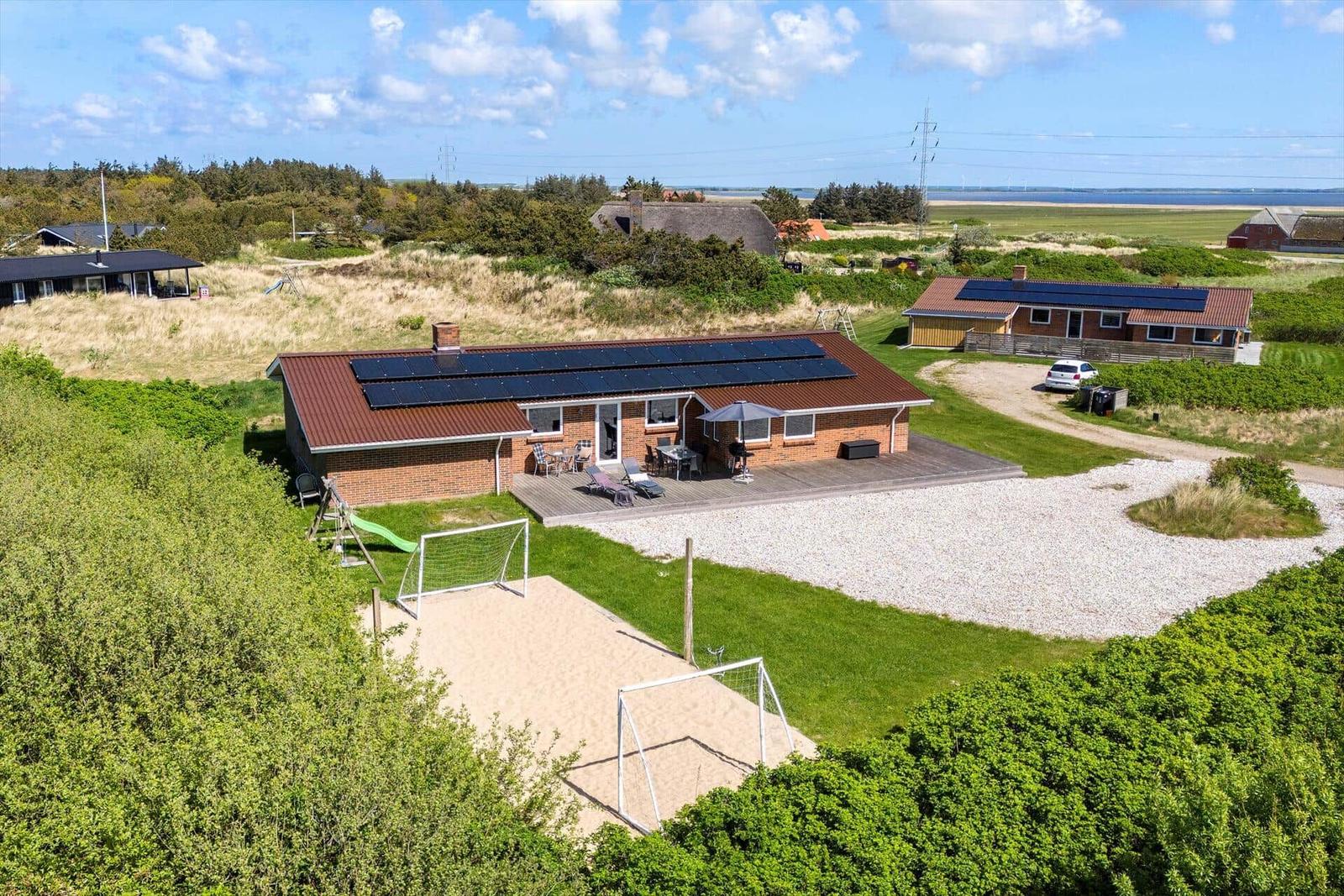 A house with solar panels, terrace, and playground in green surroundings.