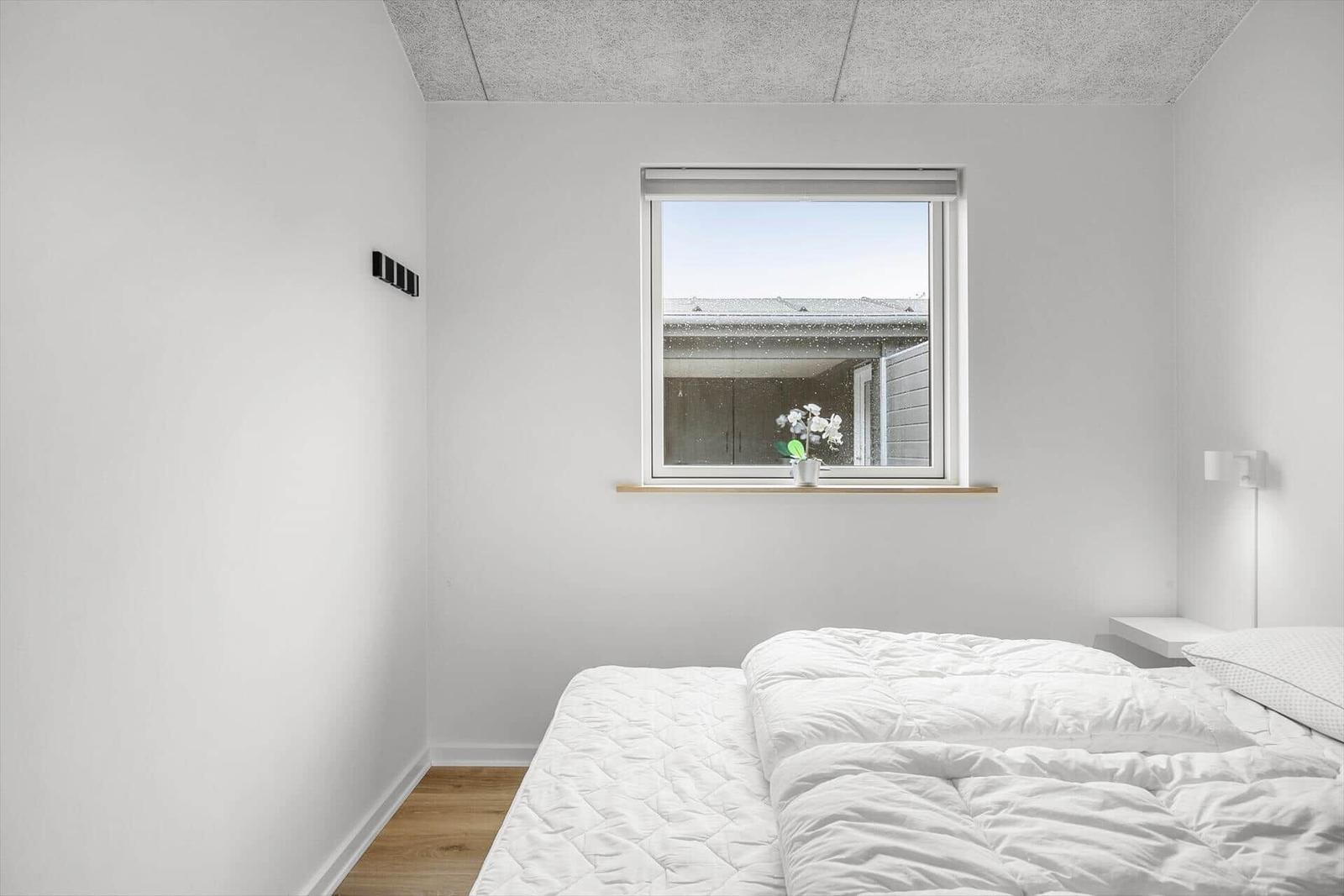 Bedroom with white bed and window. Wooden windowsill with plant.