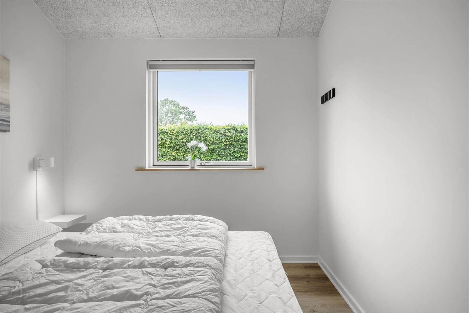 Bedroom with white bed and window view of green hedge.