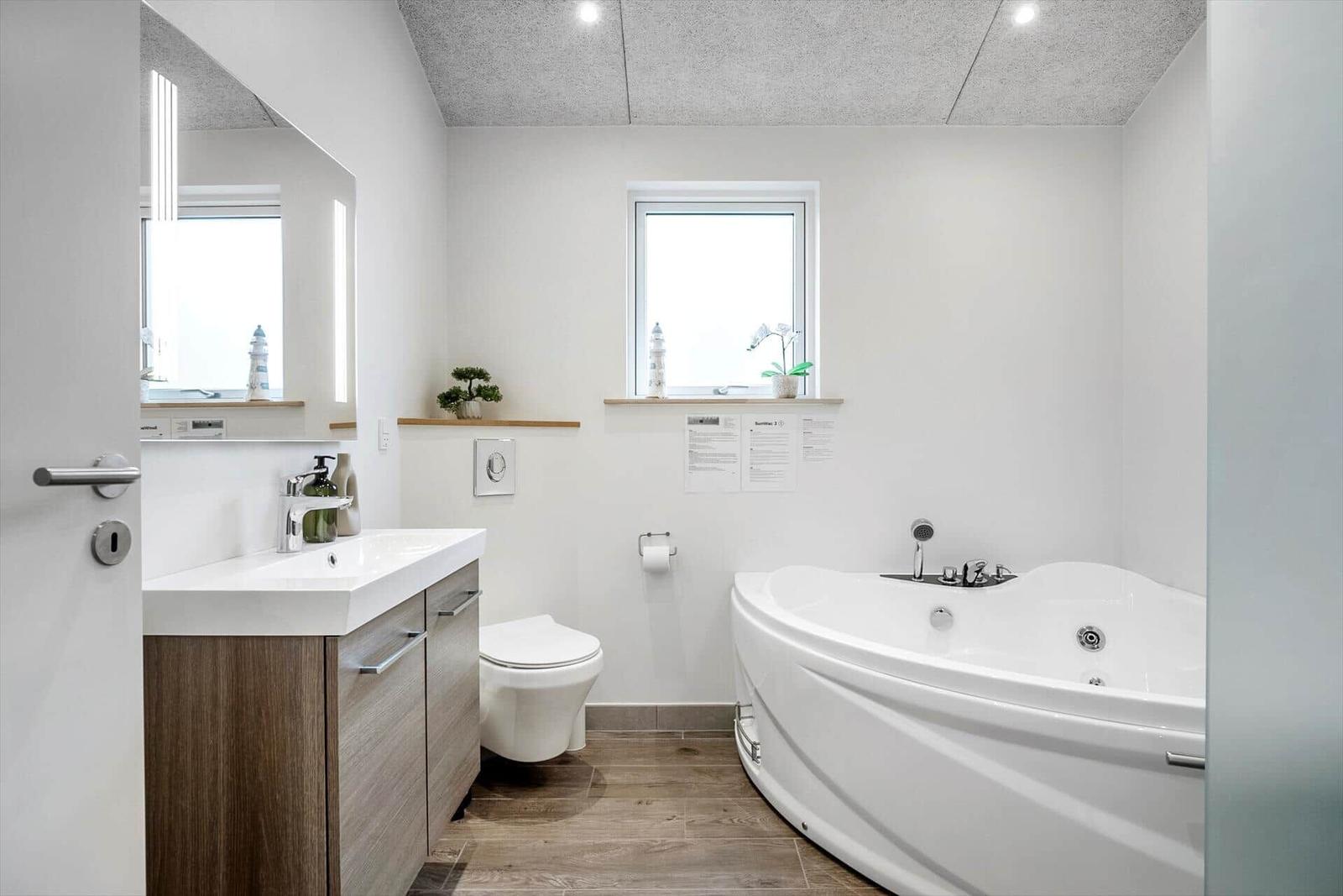 Bathroom with bathtub, sink, and toilet. Wooden floor and window.