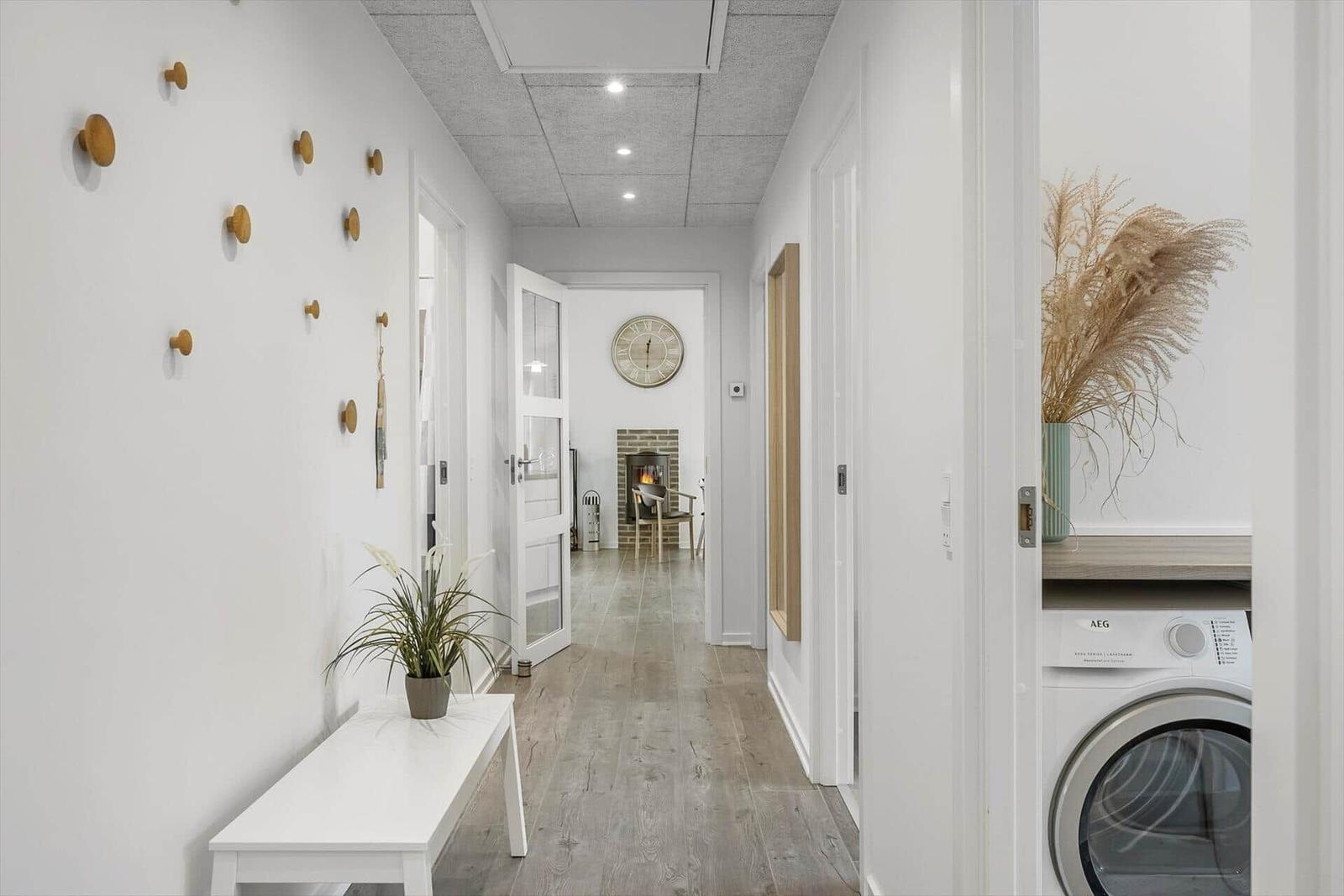 Hallway with wooden floor, coat hooks, and view into living area with fireplace.