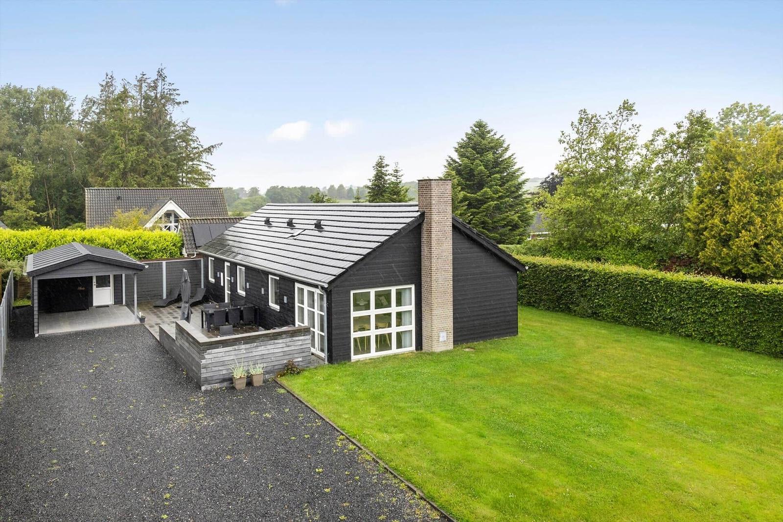Modern villa with garden, terrace, and carport. Surrounded by trees and shrubs.