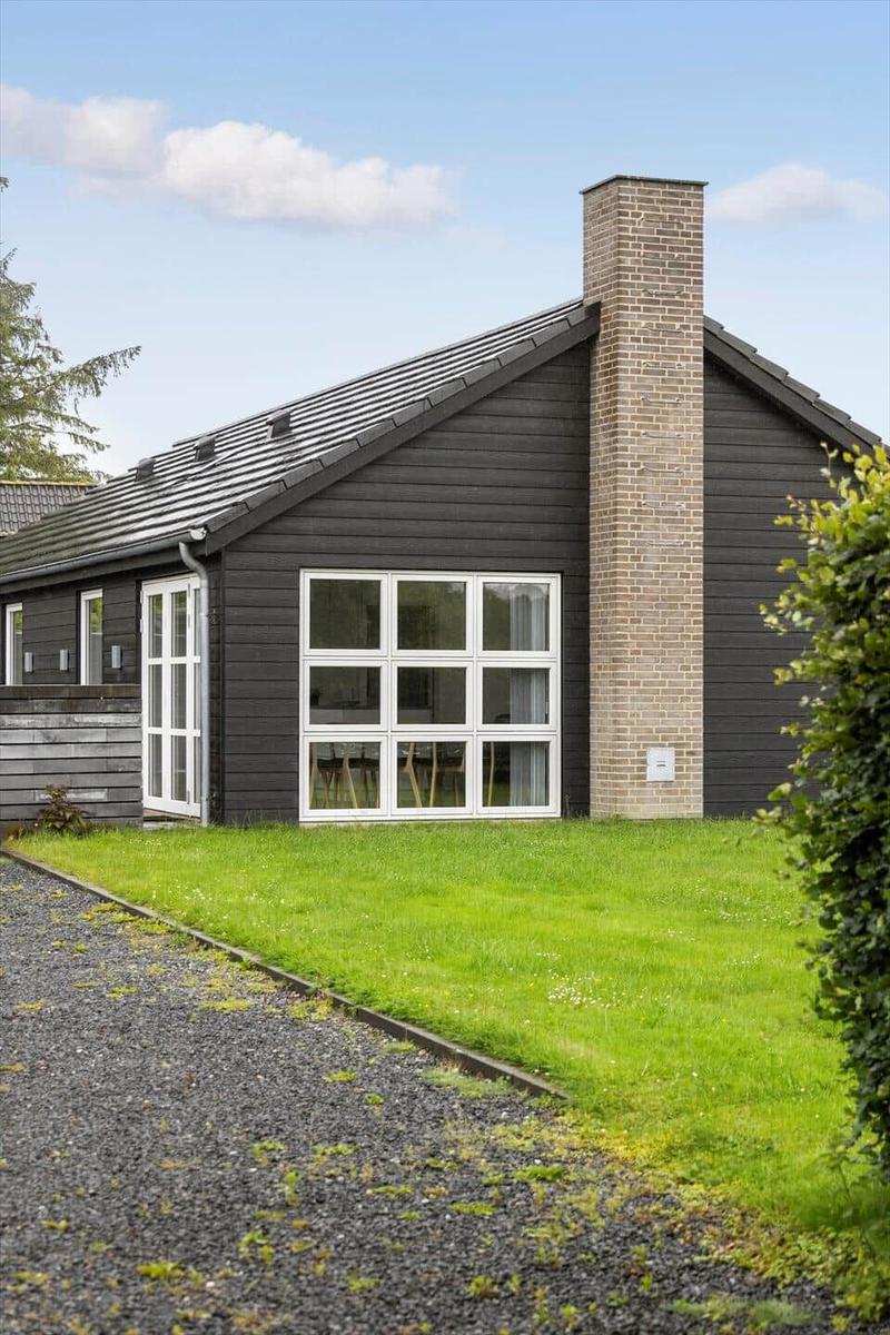 Modern villa with dark wood, large window front, and brick chimney.