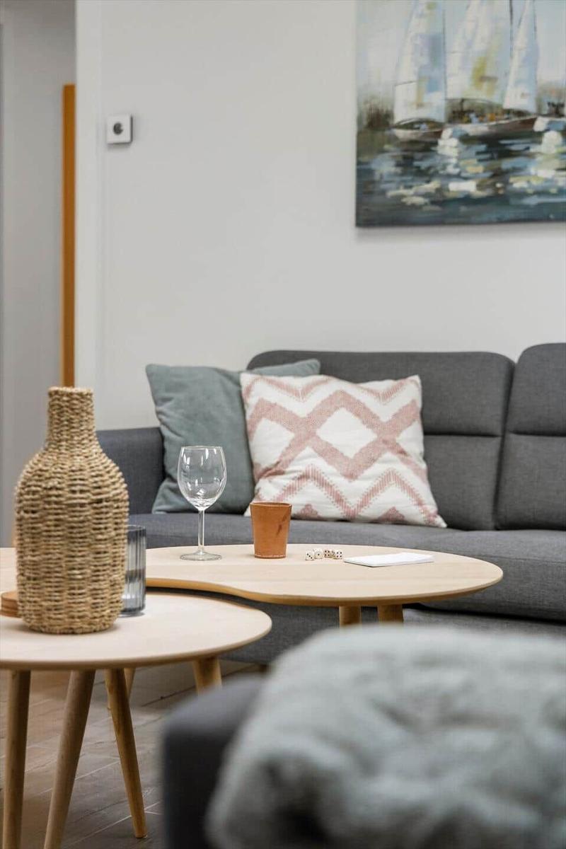 Gray sofa with cushions, round tables, and wall painting with sailboats.