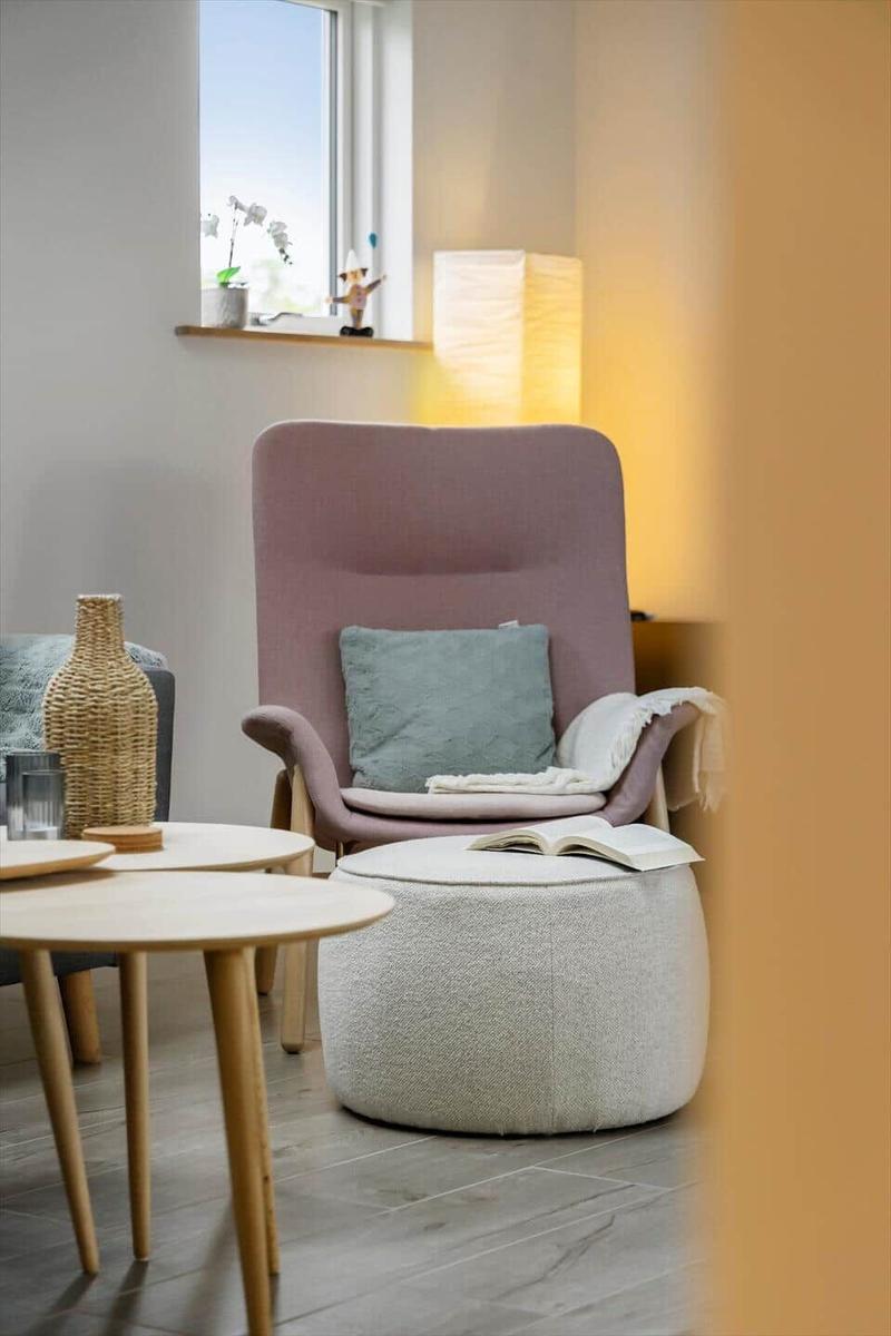 Well-lit room with pink armchair, side table, and footstool.