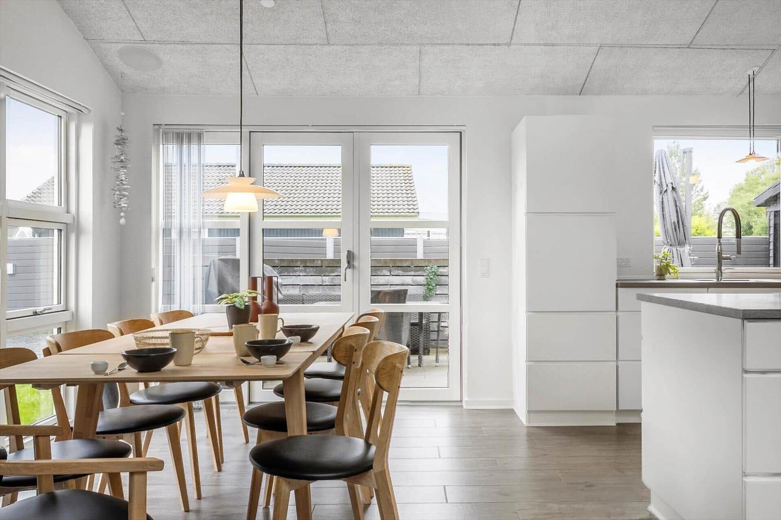 Dining area with wooden table and chairs, kitchen with countertop and windows.