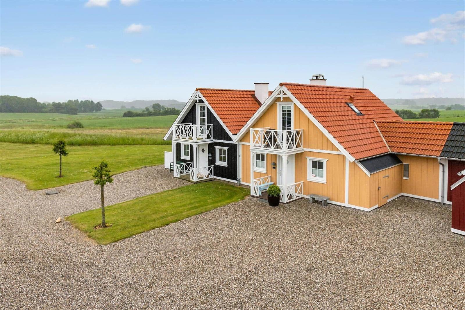 Haus mit rotem Dach und weißem Balkon auf grünem Grund.
