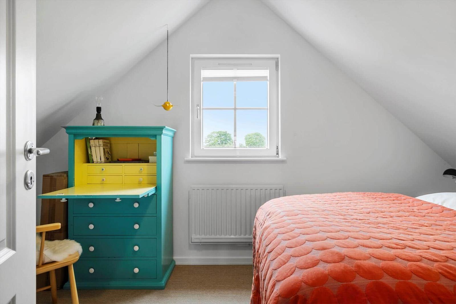 Schlafzimmer mit Dachschrägen, Fenster, Bett und Schrank.