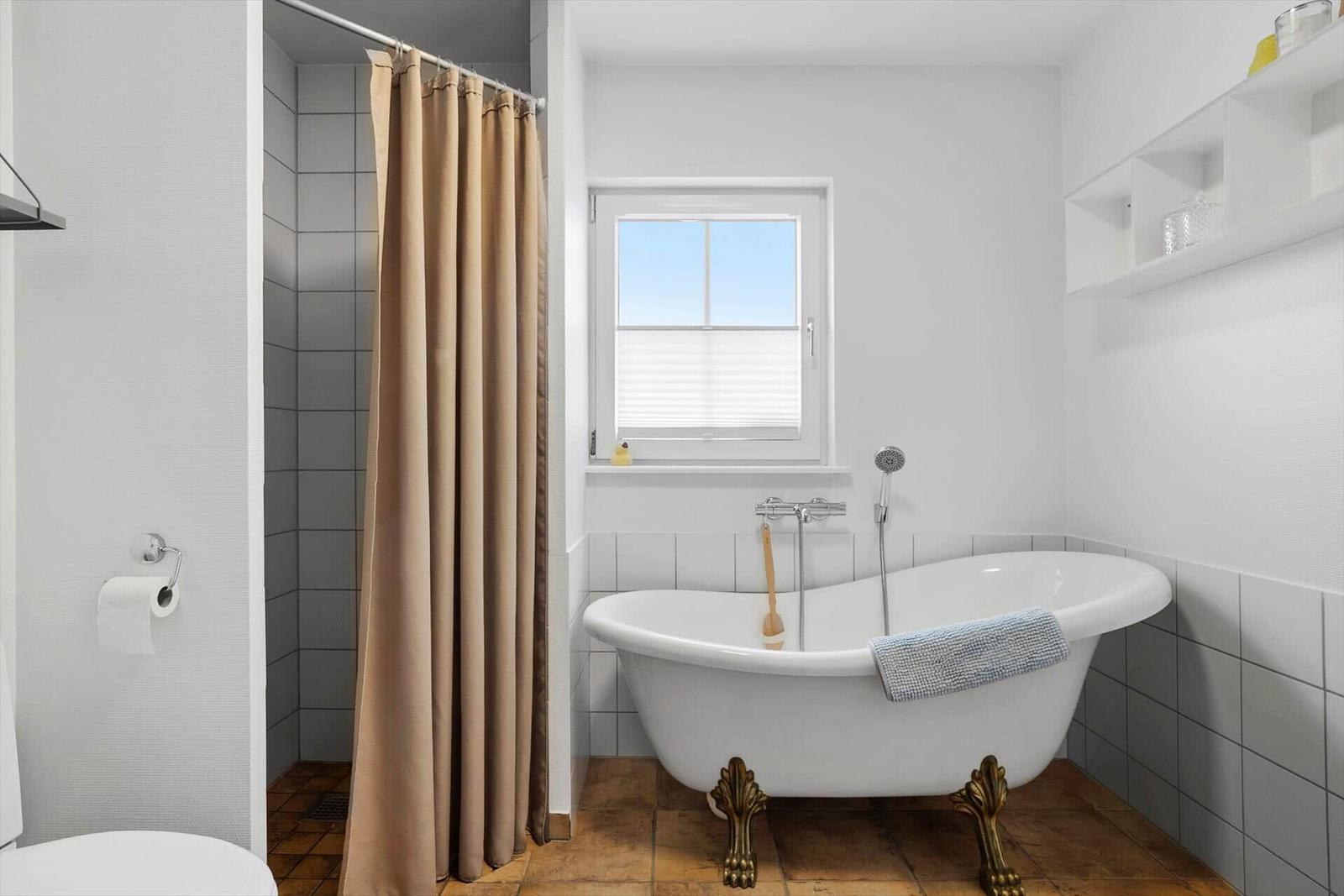 Bad mit freistehender Badewanne, Fenster und Duschvorhang.