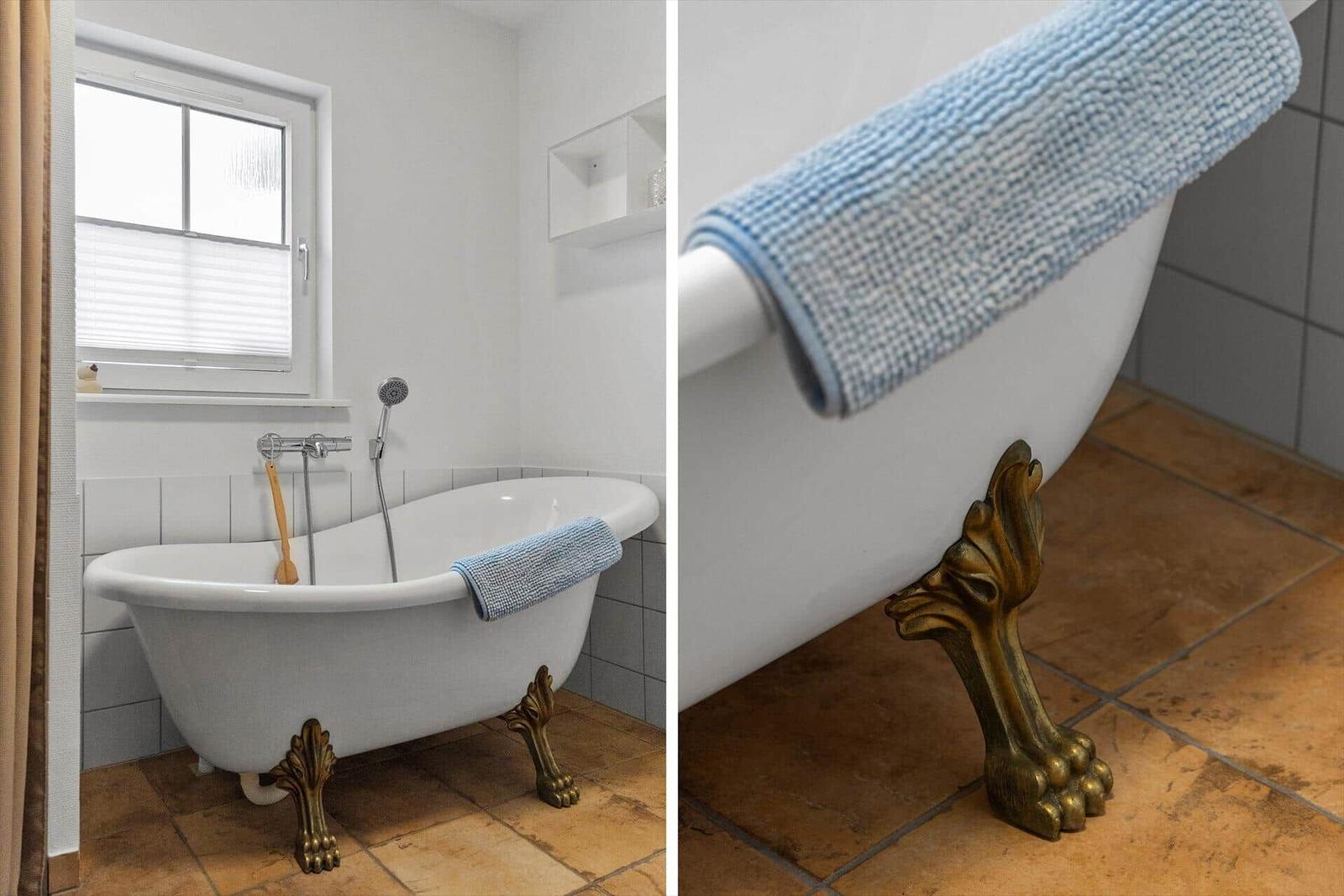 Badewanne mit goldfarbenen Füßen und blauem Handtuch auf Terrakottboden.
