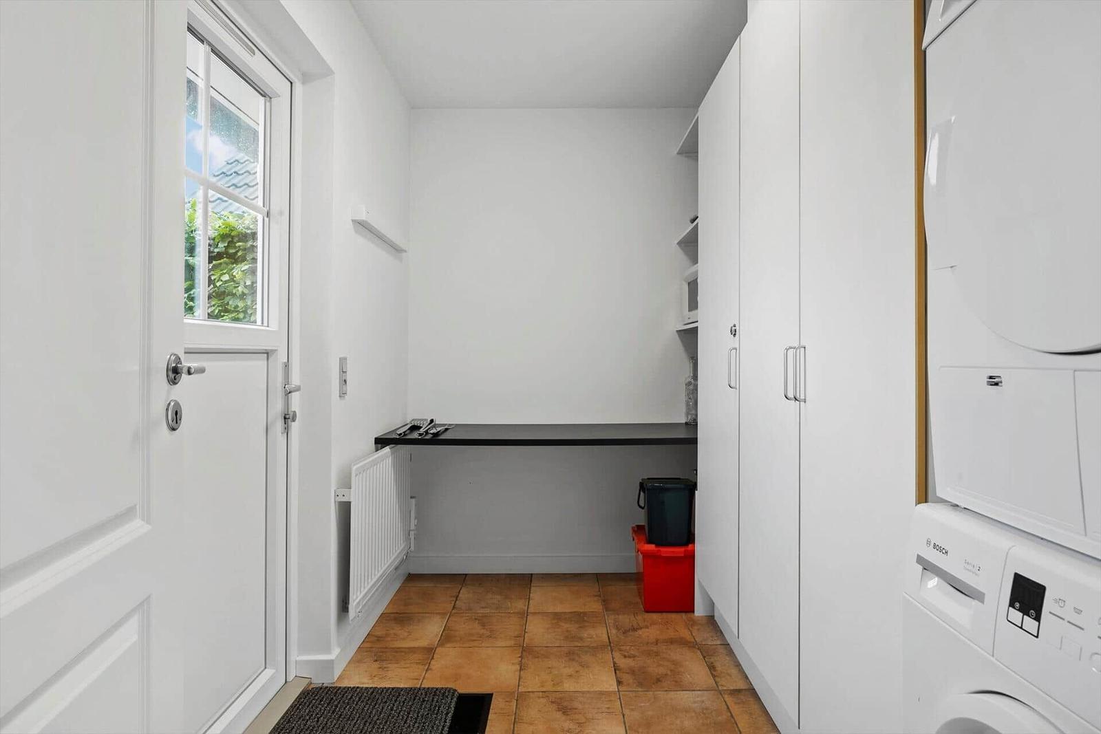 Kleiner Raum mit Waschmaschine, Schränken und Fenster zur Außenseite.