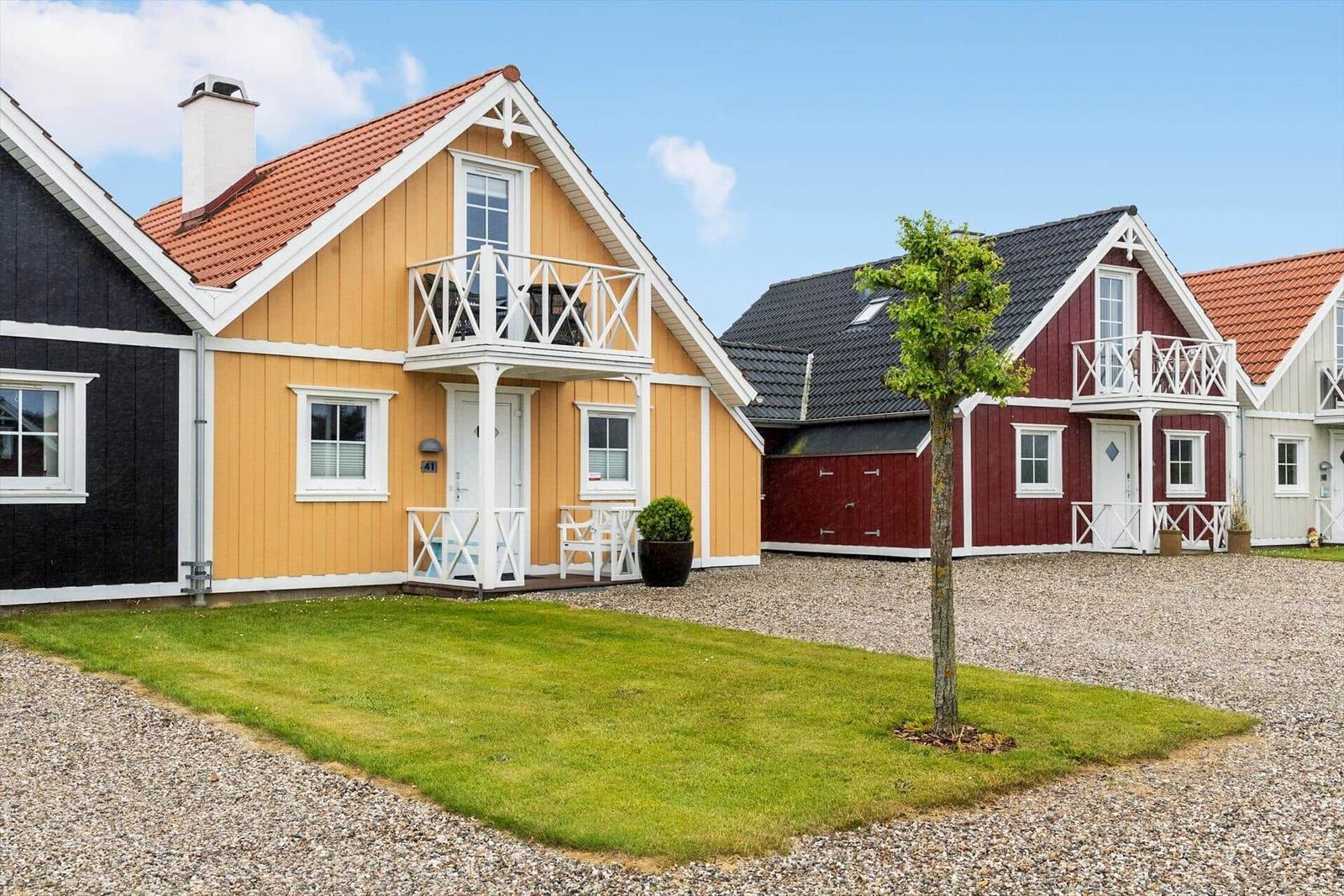 Haus mit Balkon, Grasfläche und Kiesweg. Nebenliegende Häuser in verschiedenen Farben.