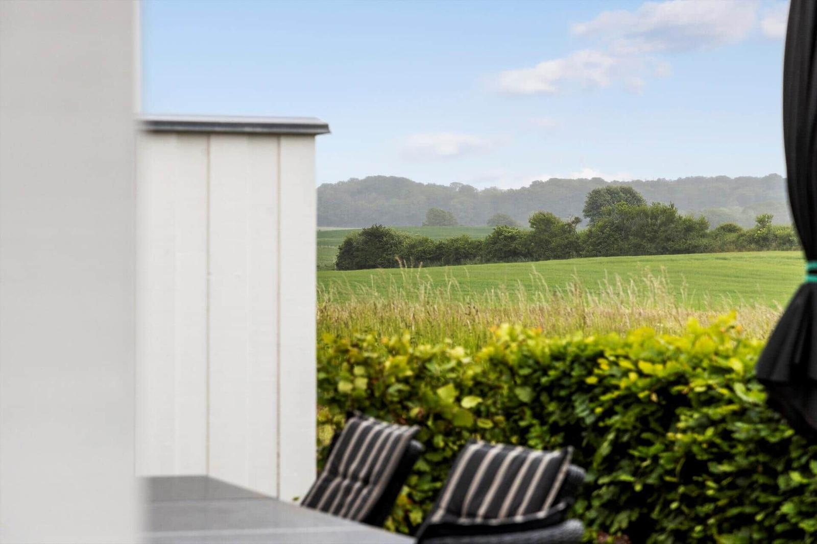 Terrasse mit Sitzgelegenheit und Blick auf grüne Wiesen und Hügel.