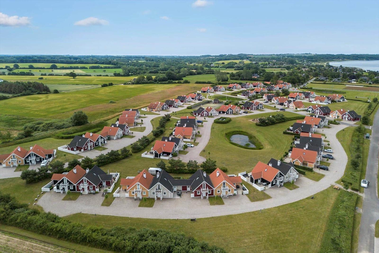 Aerial view of holiday homes with red roofs and green lawns near water.