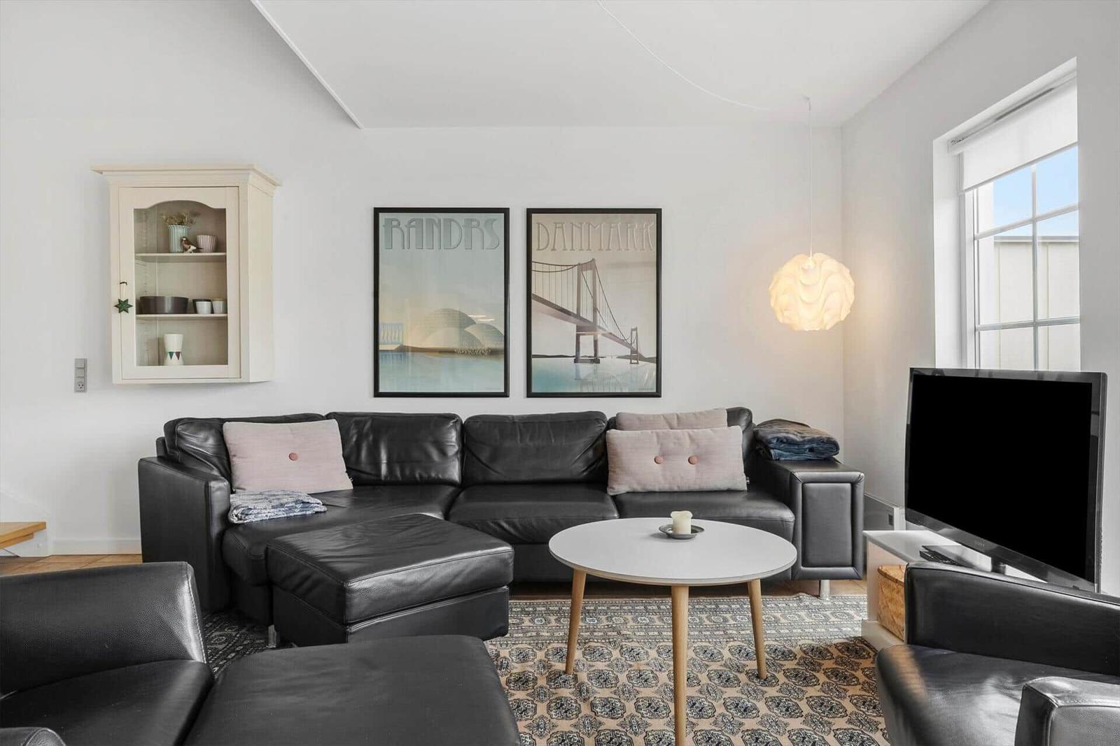 Wohnzimmer mit schwarzer Ledercouch, runden Tisch und Wandbildern.