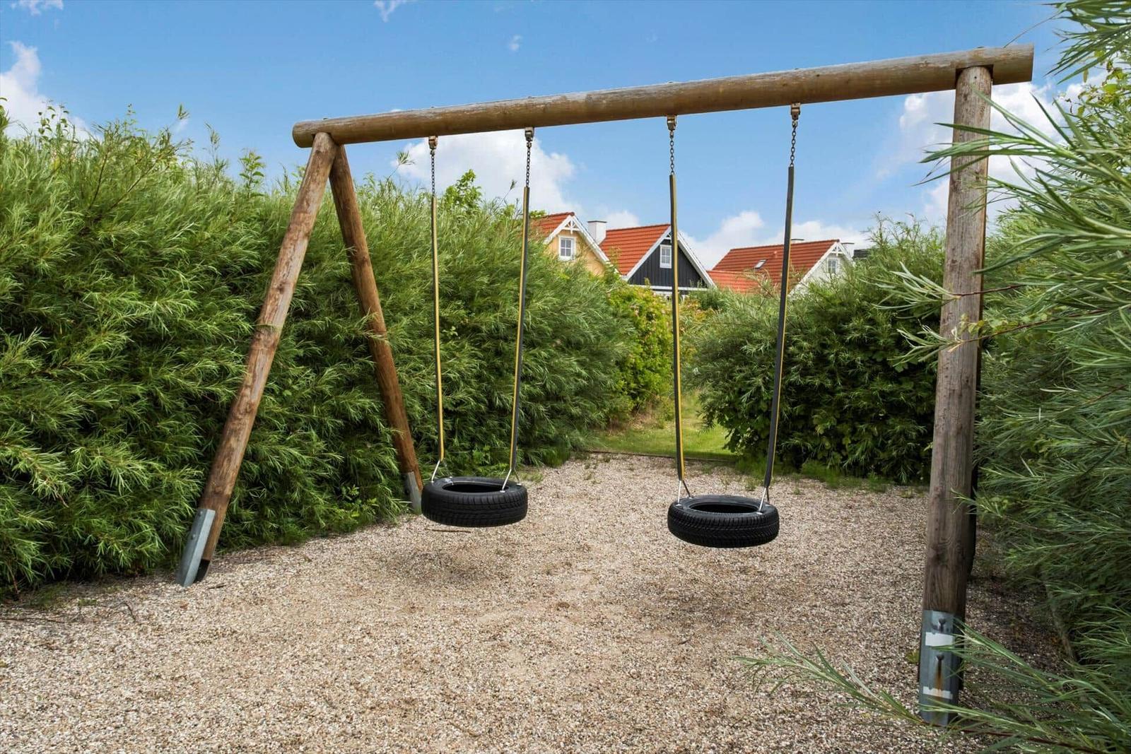 Zwei Reifen-Schaukeln auf Holzgestell im Garten mit Kies und grünen Hecken.