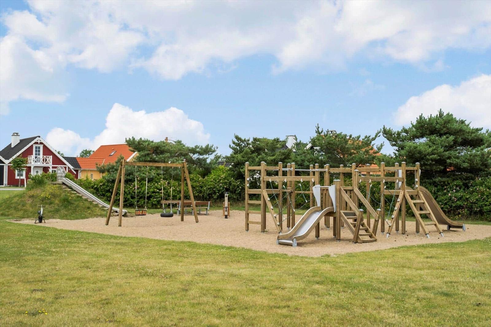 Großer Spielplatz mit Rutsche, Klettergerüst und Schaukel auf Sandfläche.