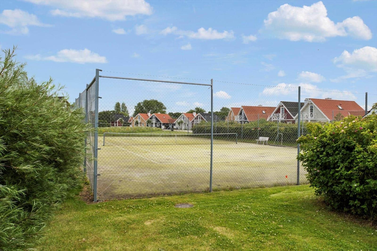 Tennisplatz hinter Zaun mit Blick auf Häuser und Grünflächen.