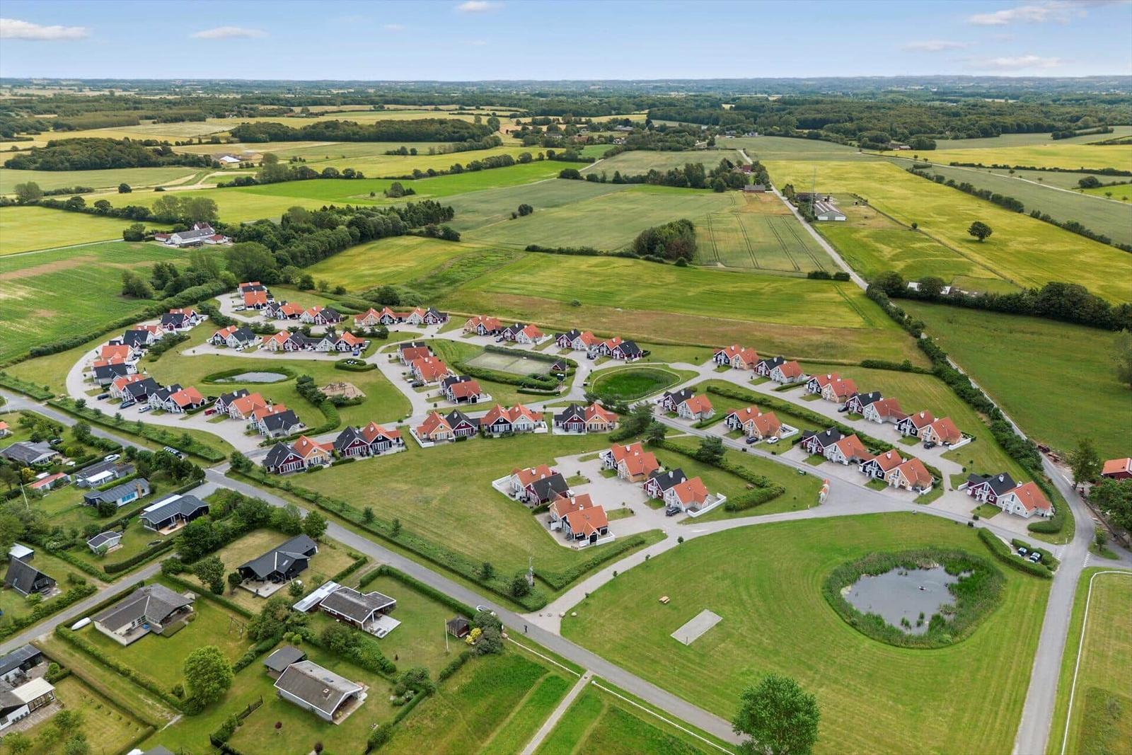 Luftbild von Wohnhäusern in einer grünen Landschaft mit Wiesen und einem Teich.