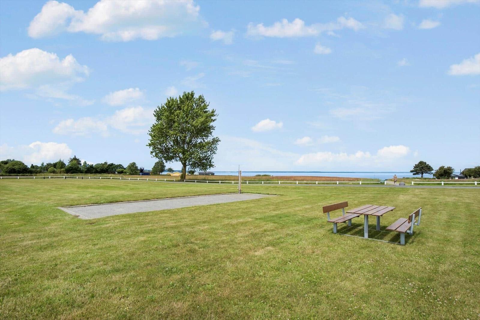 Grüner Rasenplatz mit Picknicktisch, Bäume und Blick aufs Wasser.