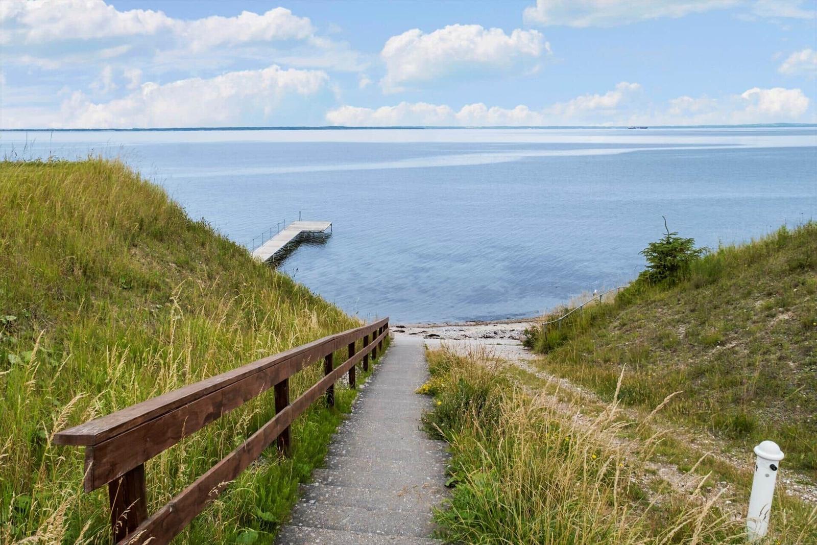 Weg mit Holzgeländer führt zum Steg am Wasser.
