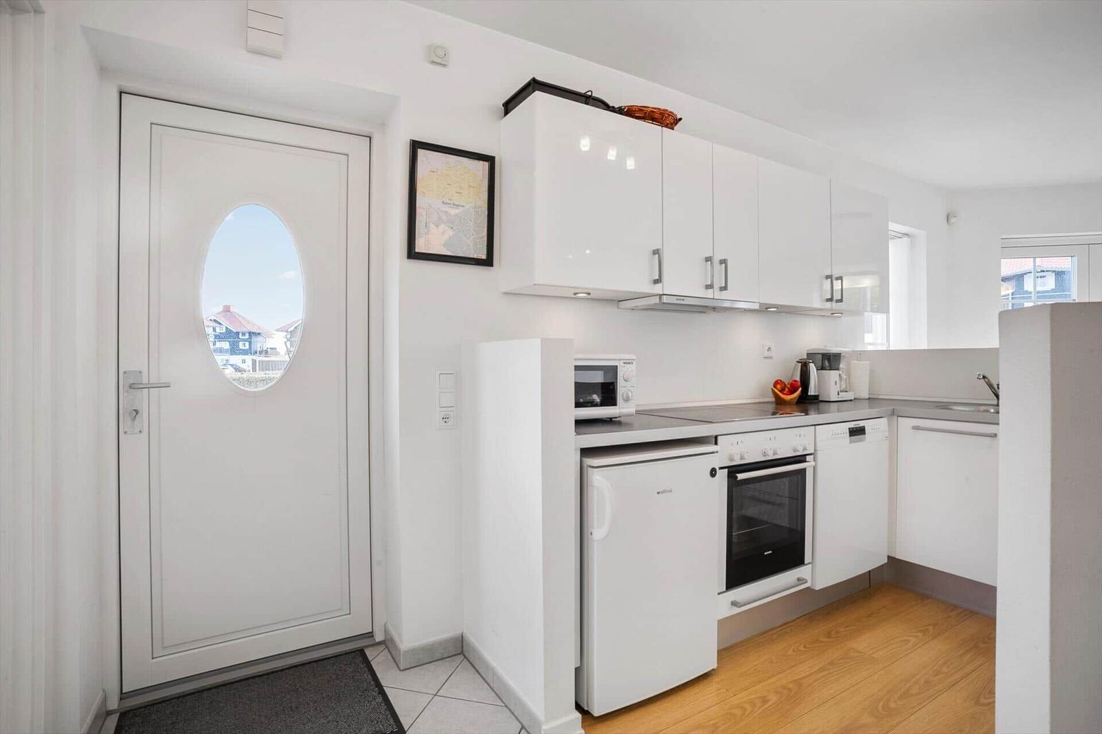 Kitchen with white cabinets, stove, fridge, and door with round window.