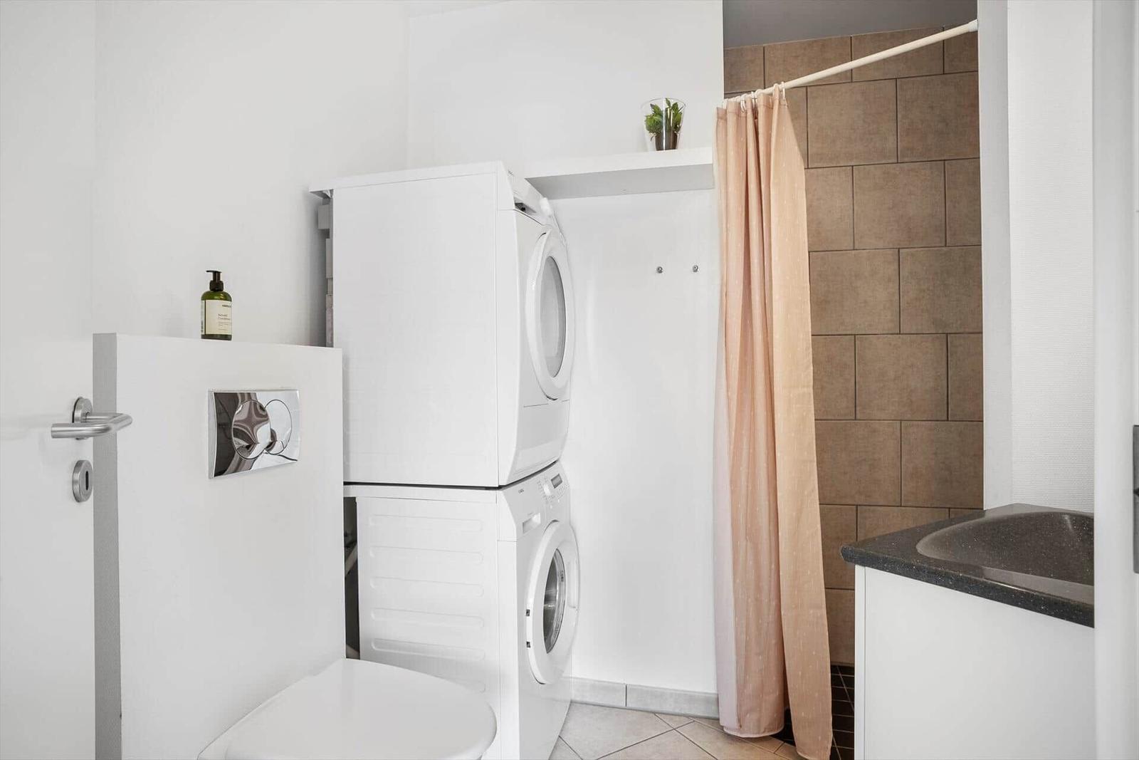 Washing machine and dryer are stacked. Shower with curtain and sink.