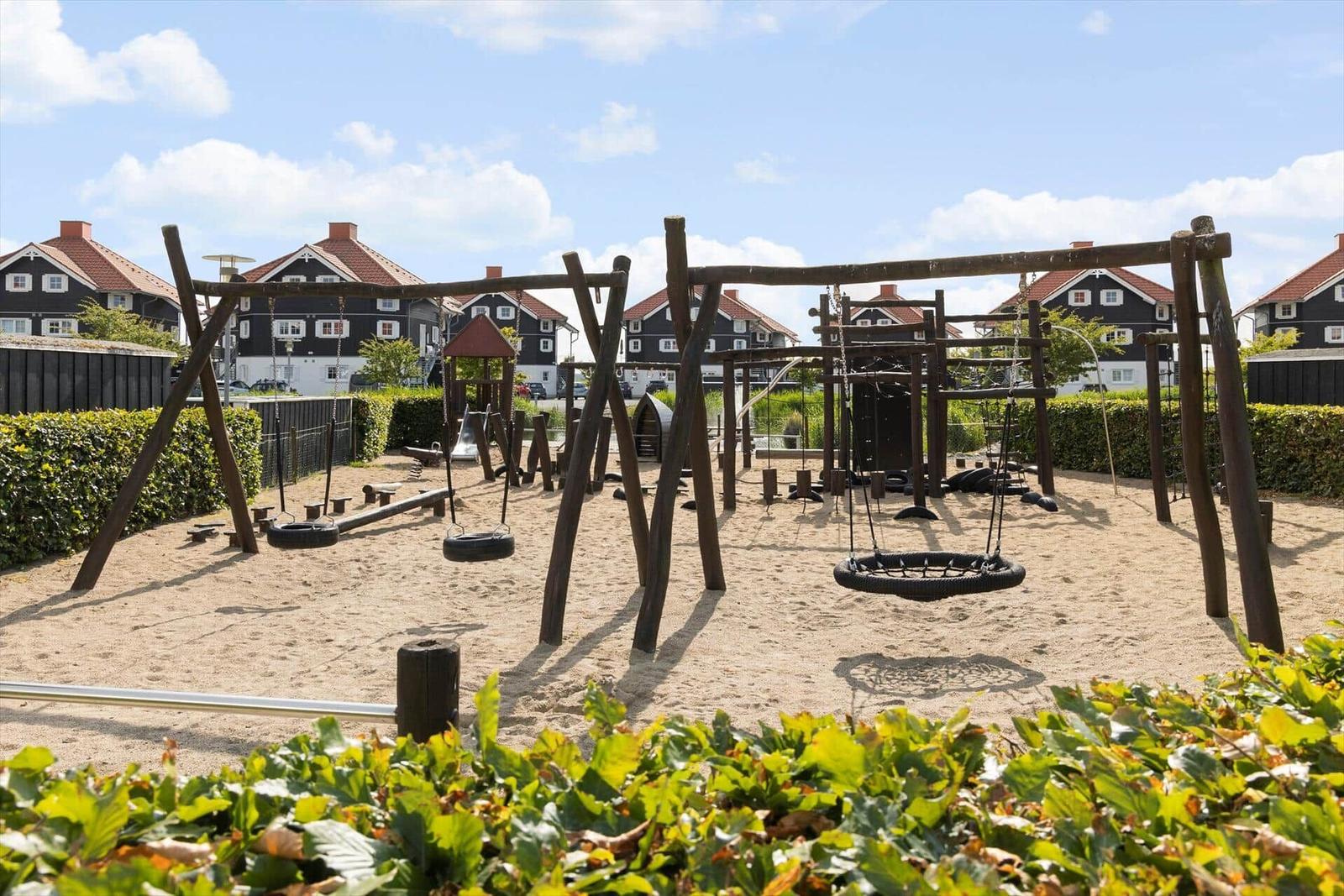 Large sandy playground with wooden play equipment and rope swings for children.