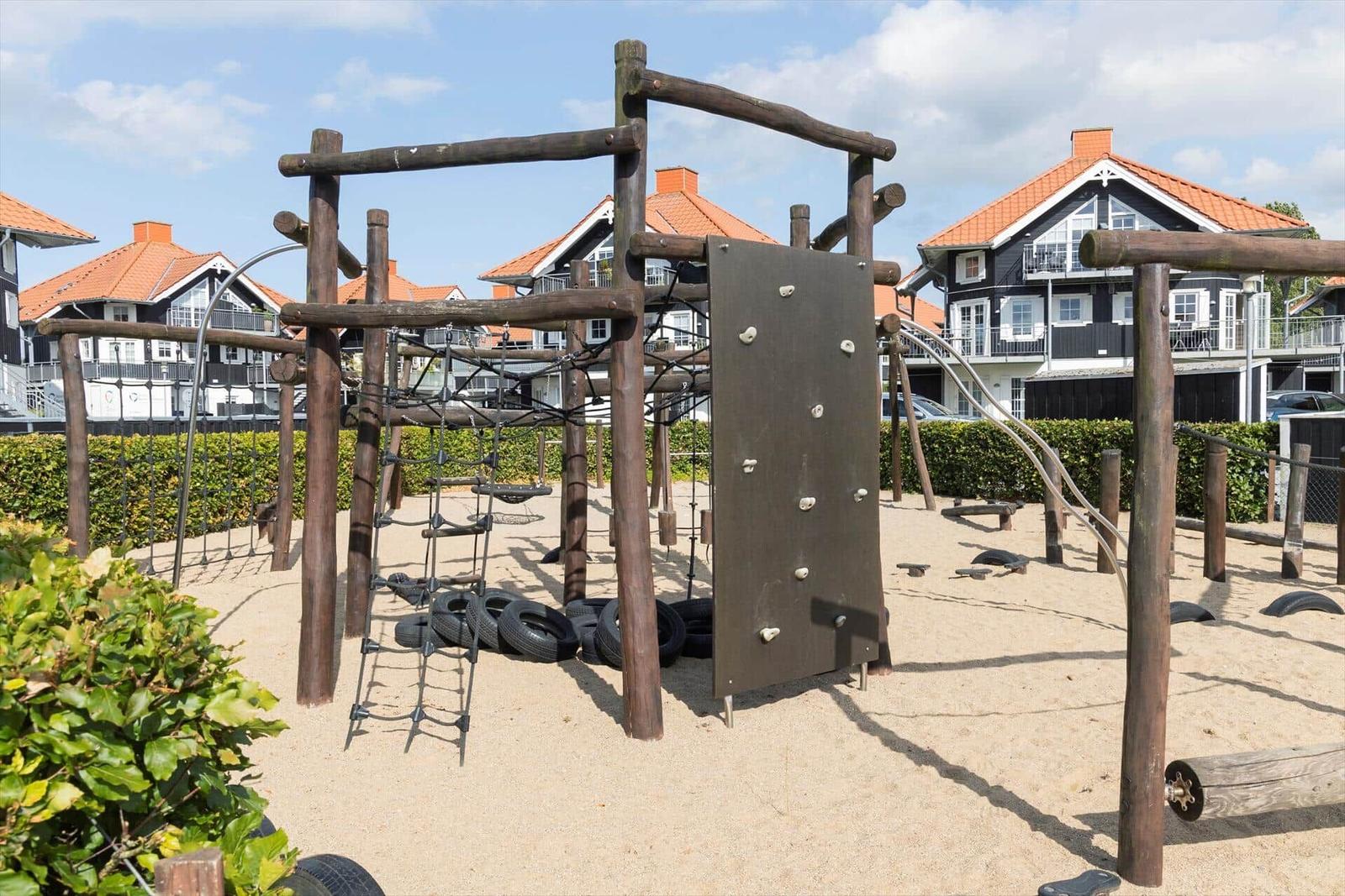 Wooden playground with climbing wall and tires on sand surface