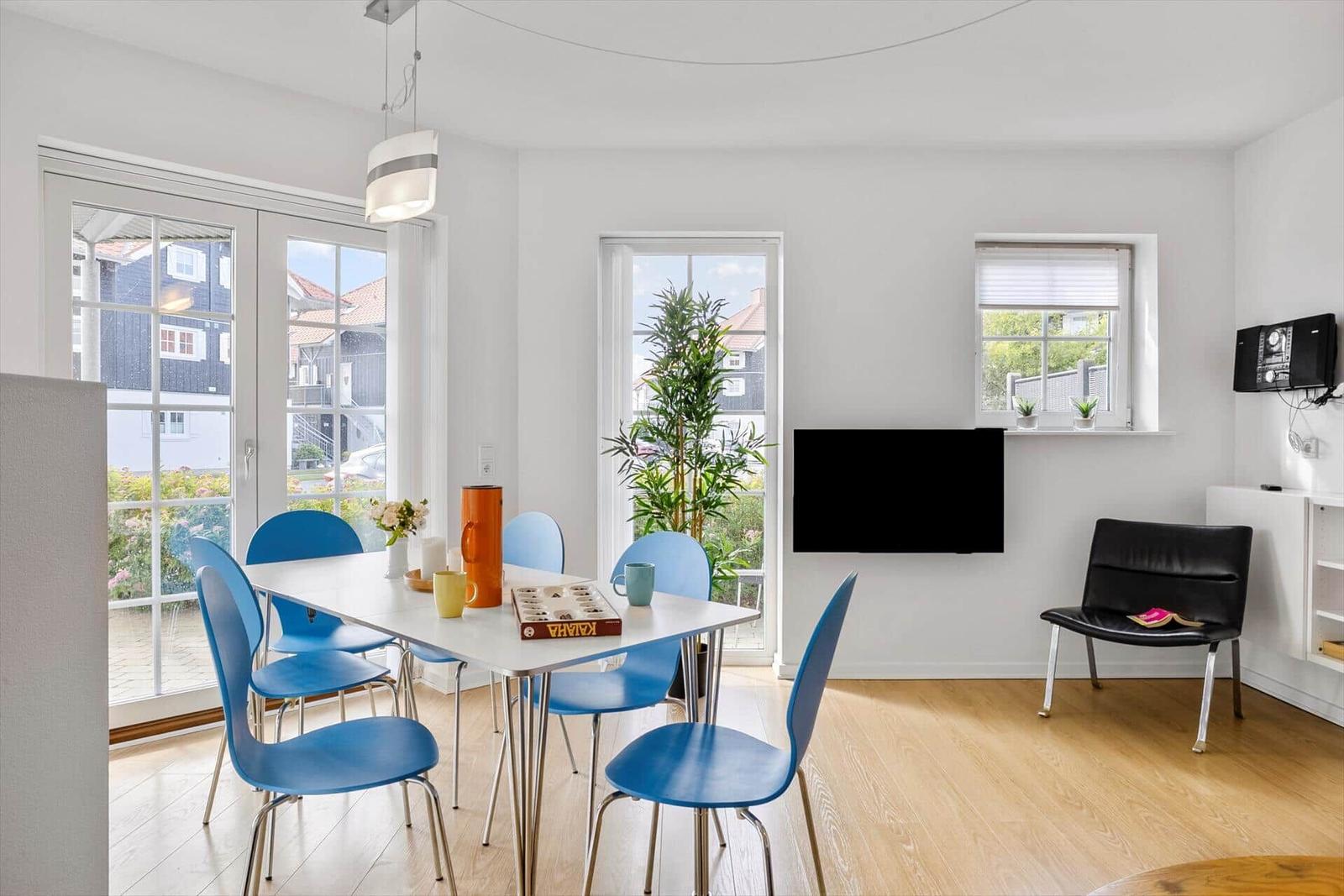 Dining area with blue chairs, TV, and windows overlooking outside.