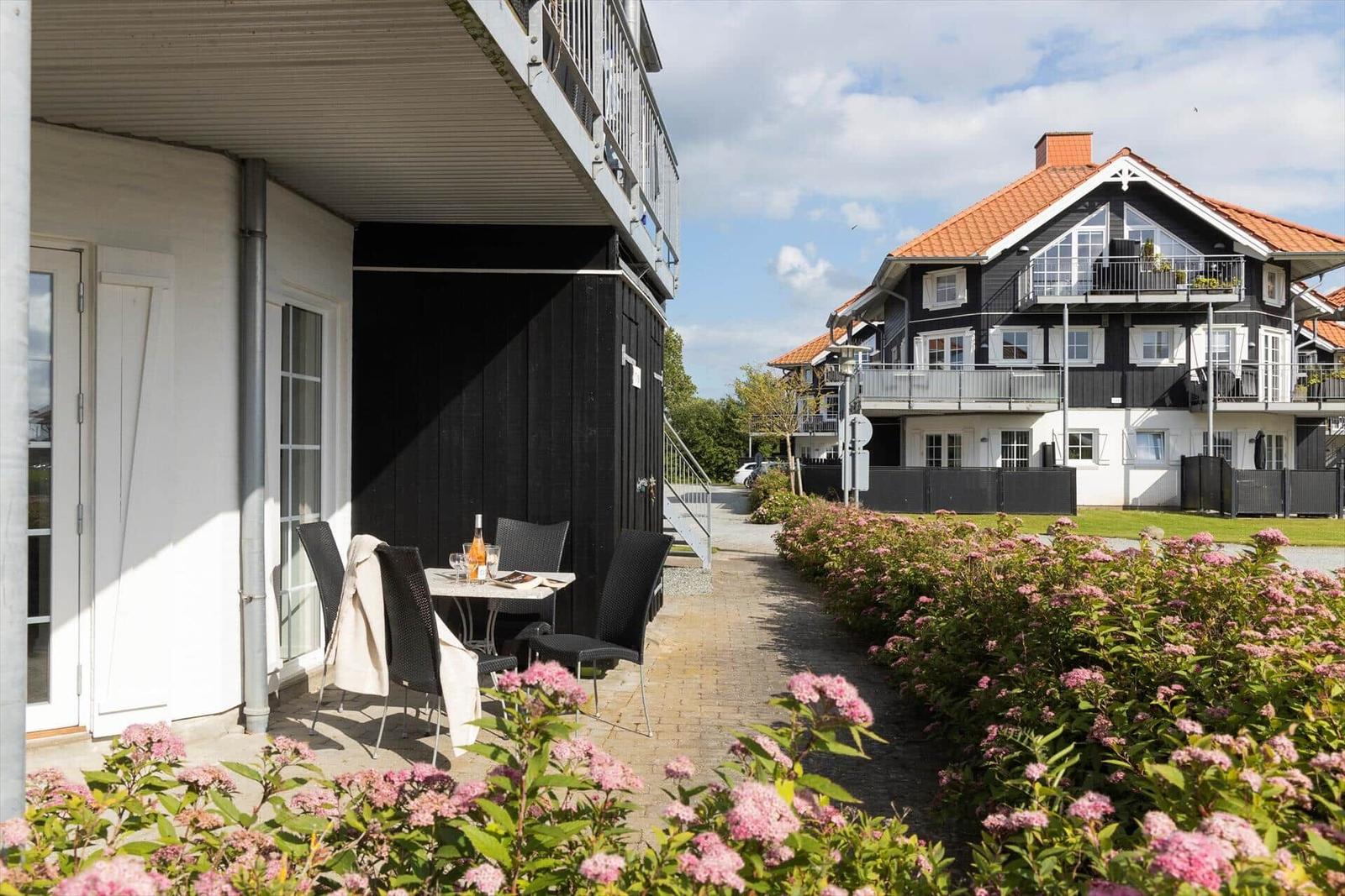 Terrace with table and chairs next to a house with flower beds.