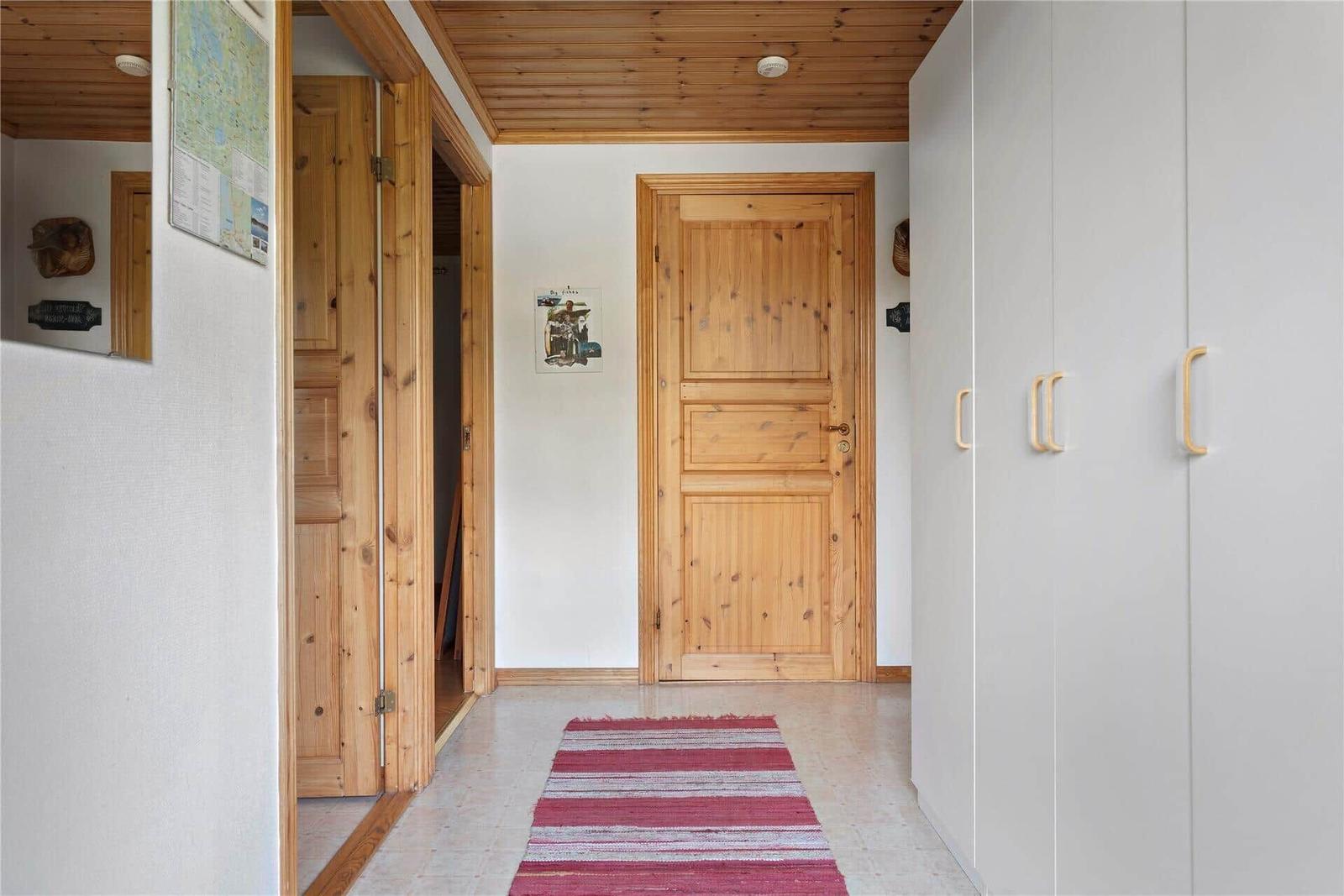 Hallway with wooden ceiling, white walls, wooden doors, and a red rug.