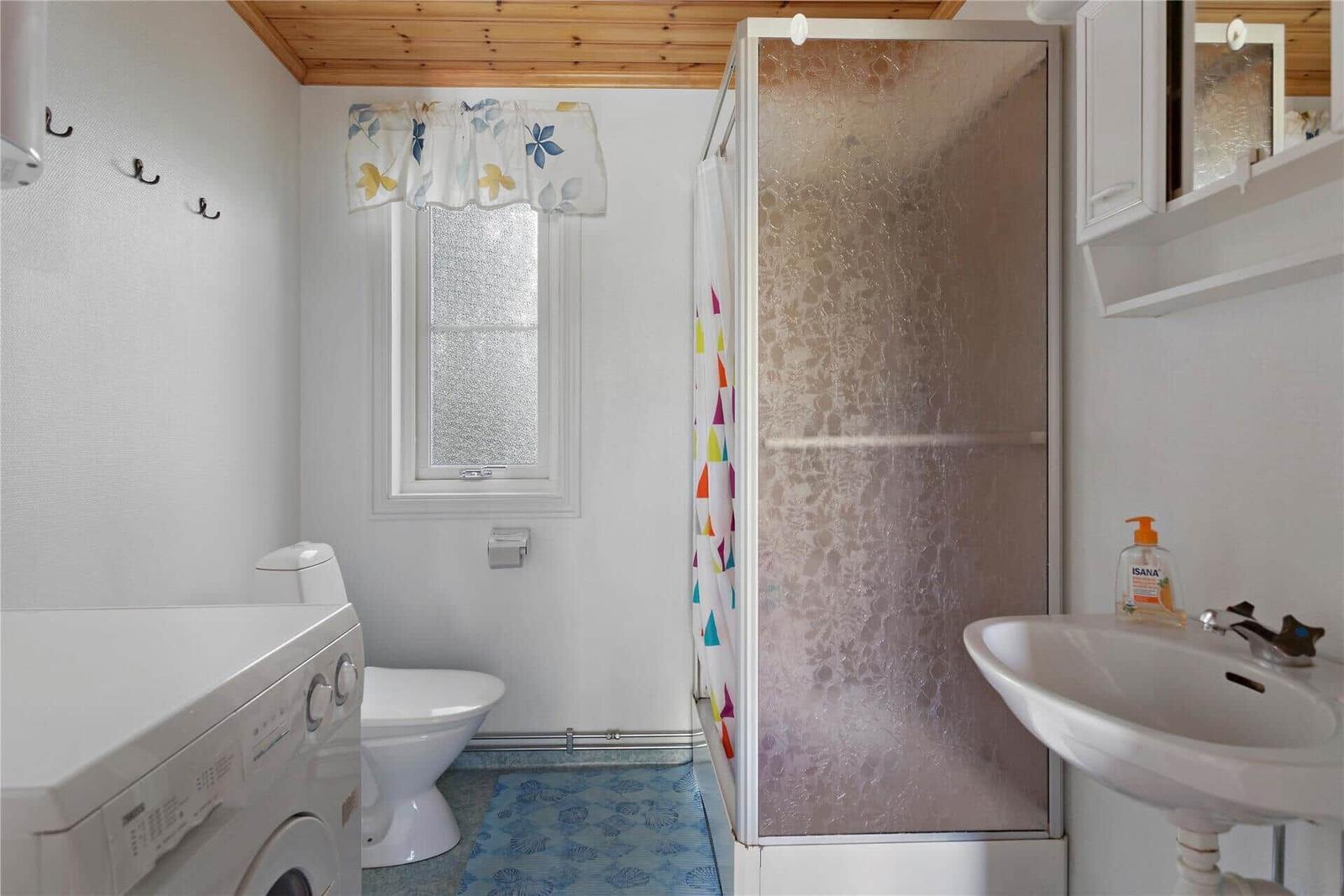 Bathroom with shower, sink, and toilet. Window with curtain and washing machine.