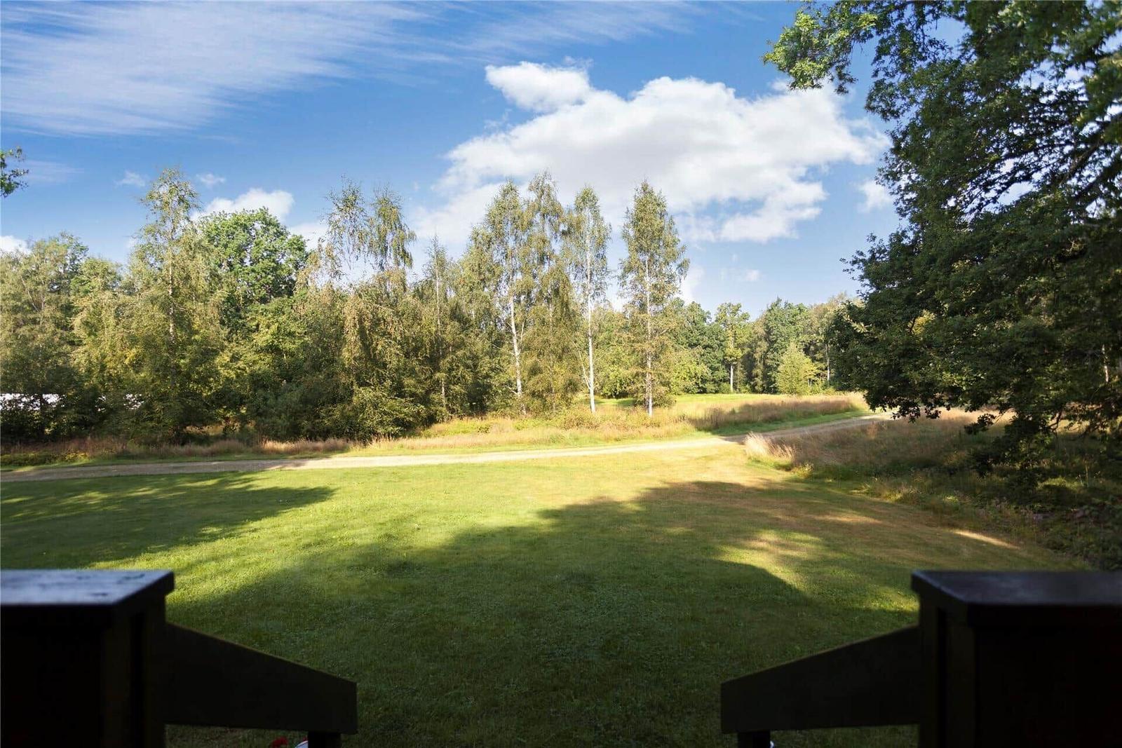 Green lawn area with forest and blue sky. Wooden railing in foreground.