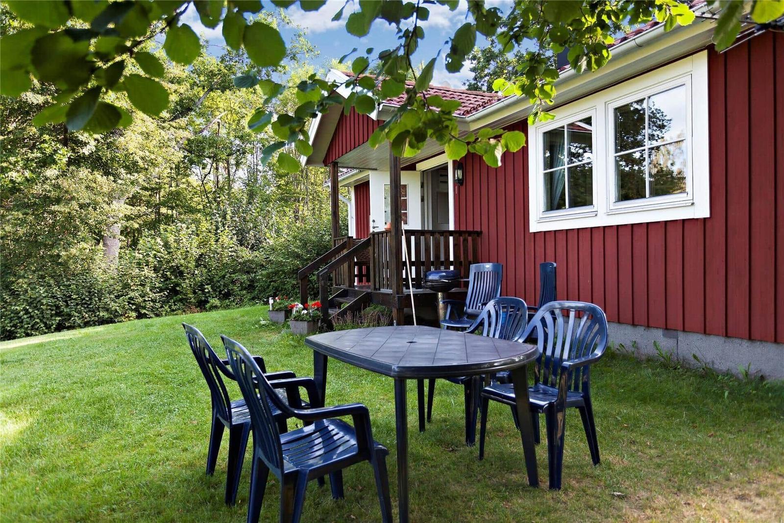 Red wooden house with porch and garden furniture under trees.